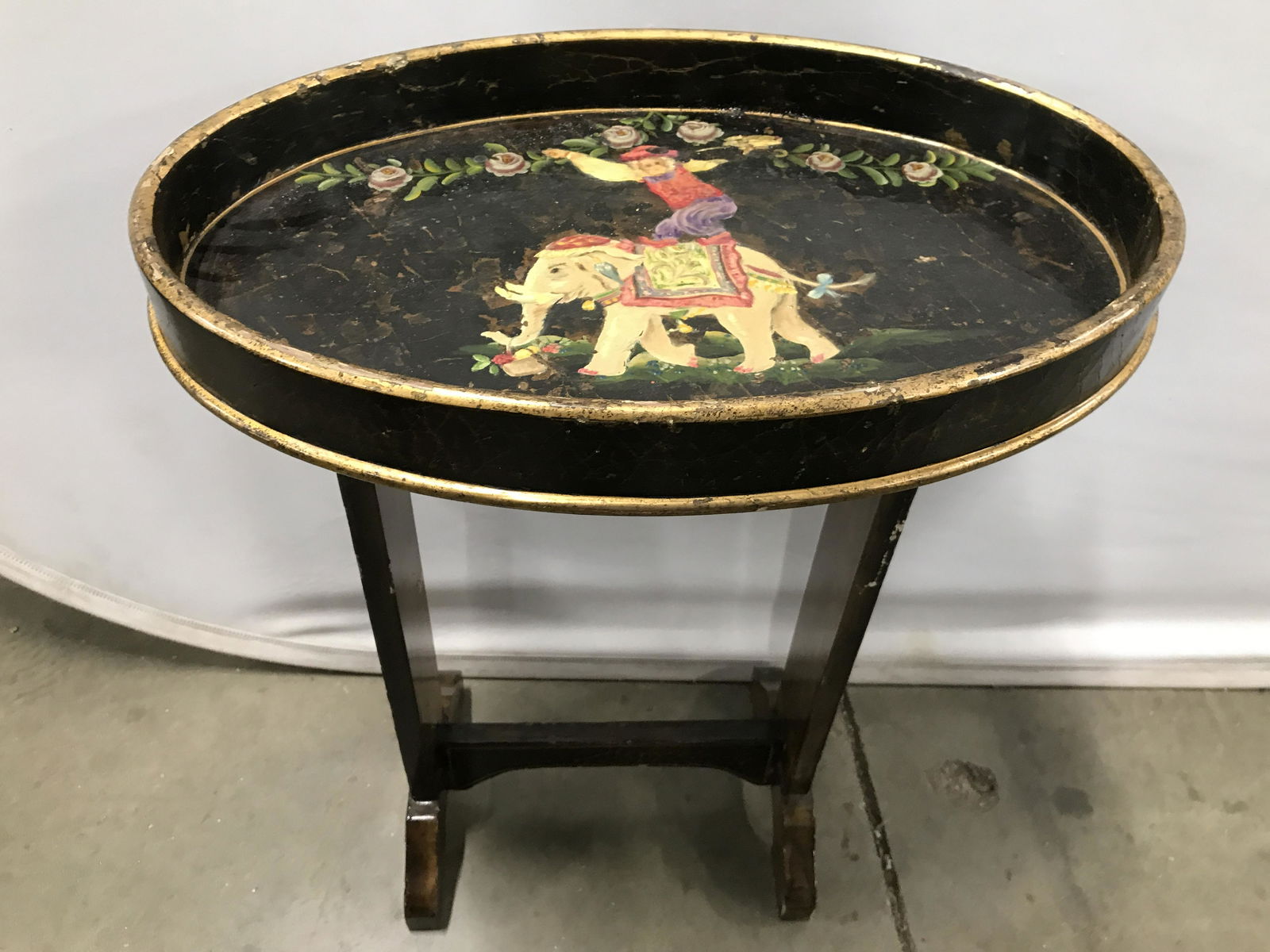 Vintage Hand Painted Wooden Tray Top Table: Table is vintage possibly antique. Piece contains hand painted detail depicting a figure standing on an elephant along with floral vine and leaf detail. Table top is oval shaped and not attached to ba