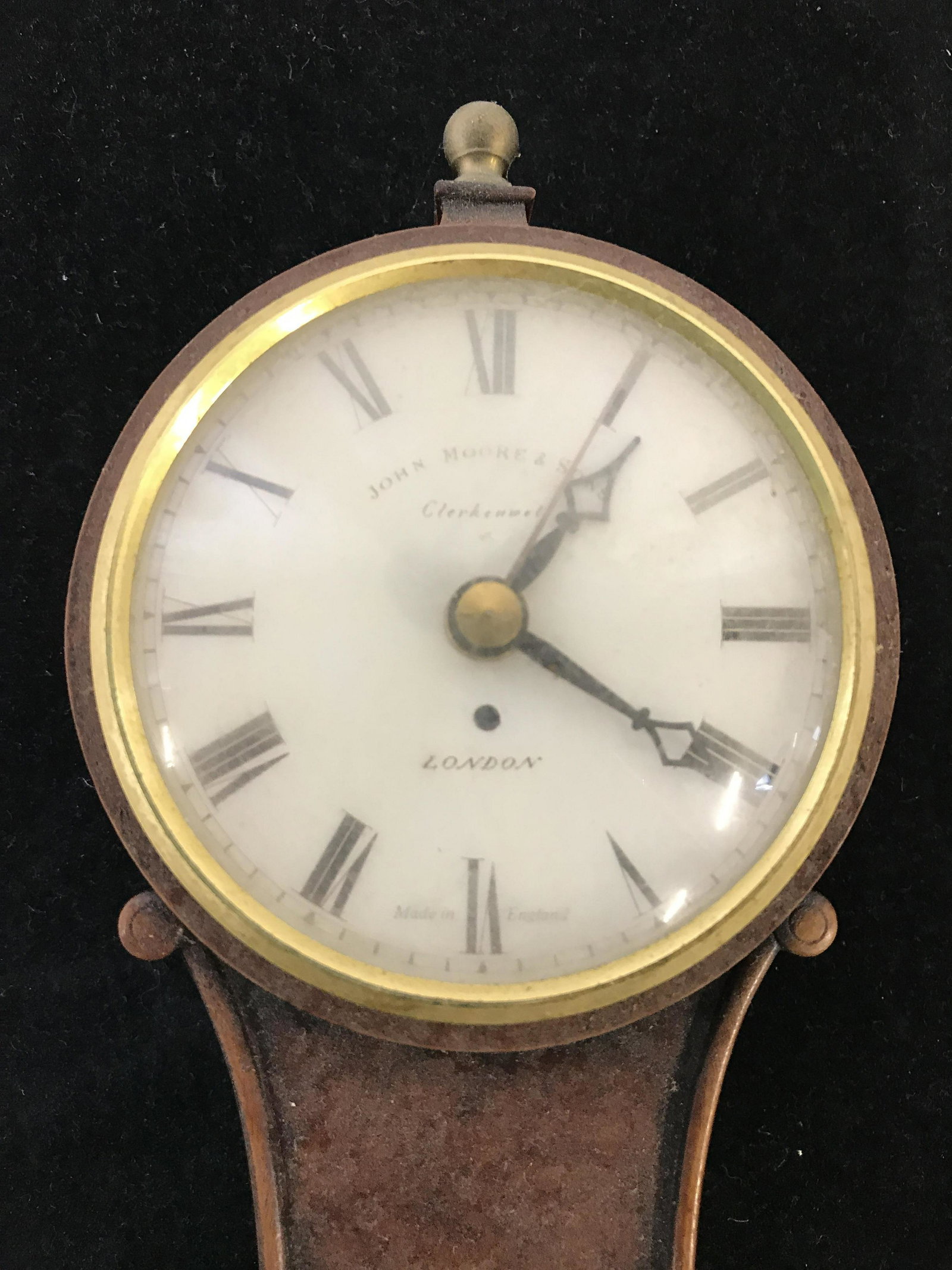 Vintage JOHN MOORE & SONS Wall Clock: Wall clock is brown toned, possibly wooden. Piece has white toned Clockface with black toned hands & Roman numerals. Face reads JOHN MOORE& SONS. Piece measures approximately 15 inches tall 4 inches w