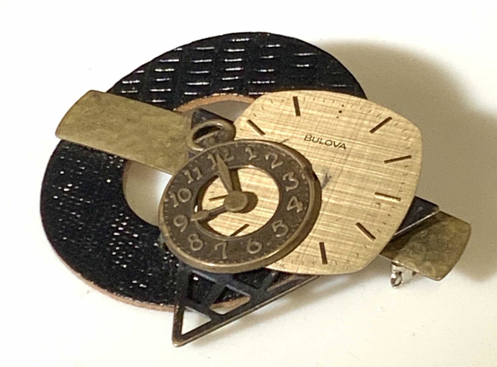 Signed Bulova Clock Themed Brooch: Black fabric and gold toned clock/watch themed brooch. Black fabric circle adorned with clock and clock face. Clock face reads: BULOVA, Quartz, Swiss 7049. The clock face is moveable. Condition consis