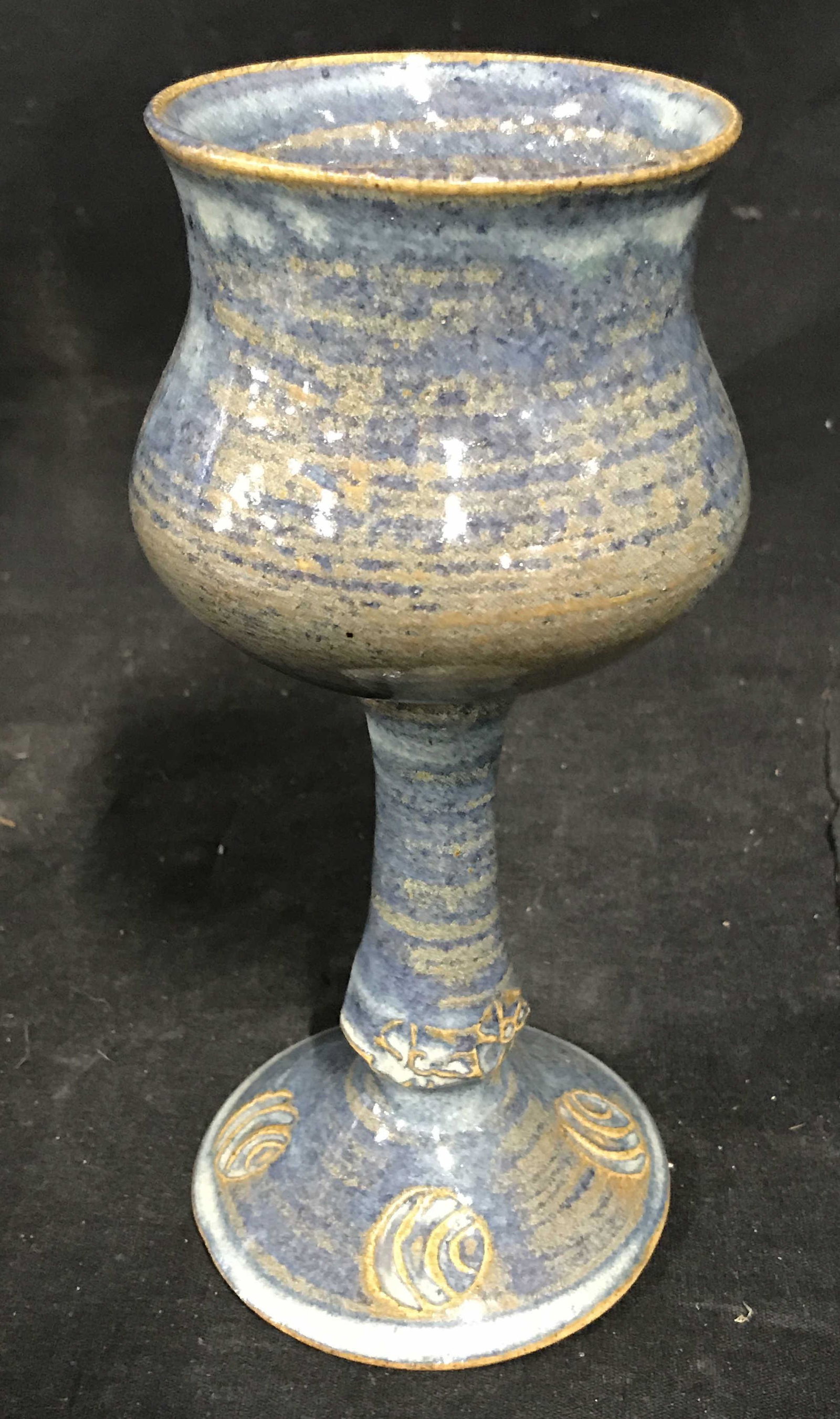 Ceramic Blue Glazed Chalice Vessel: Ceramic blue chalice, glazed and polished surface, unglazed bottom, piece colored blue and brown, circular style designs to the base of the piece, measures 7.75 inches at tallest point, Ceramic, ceram