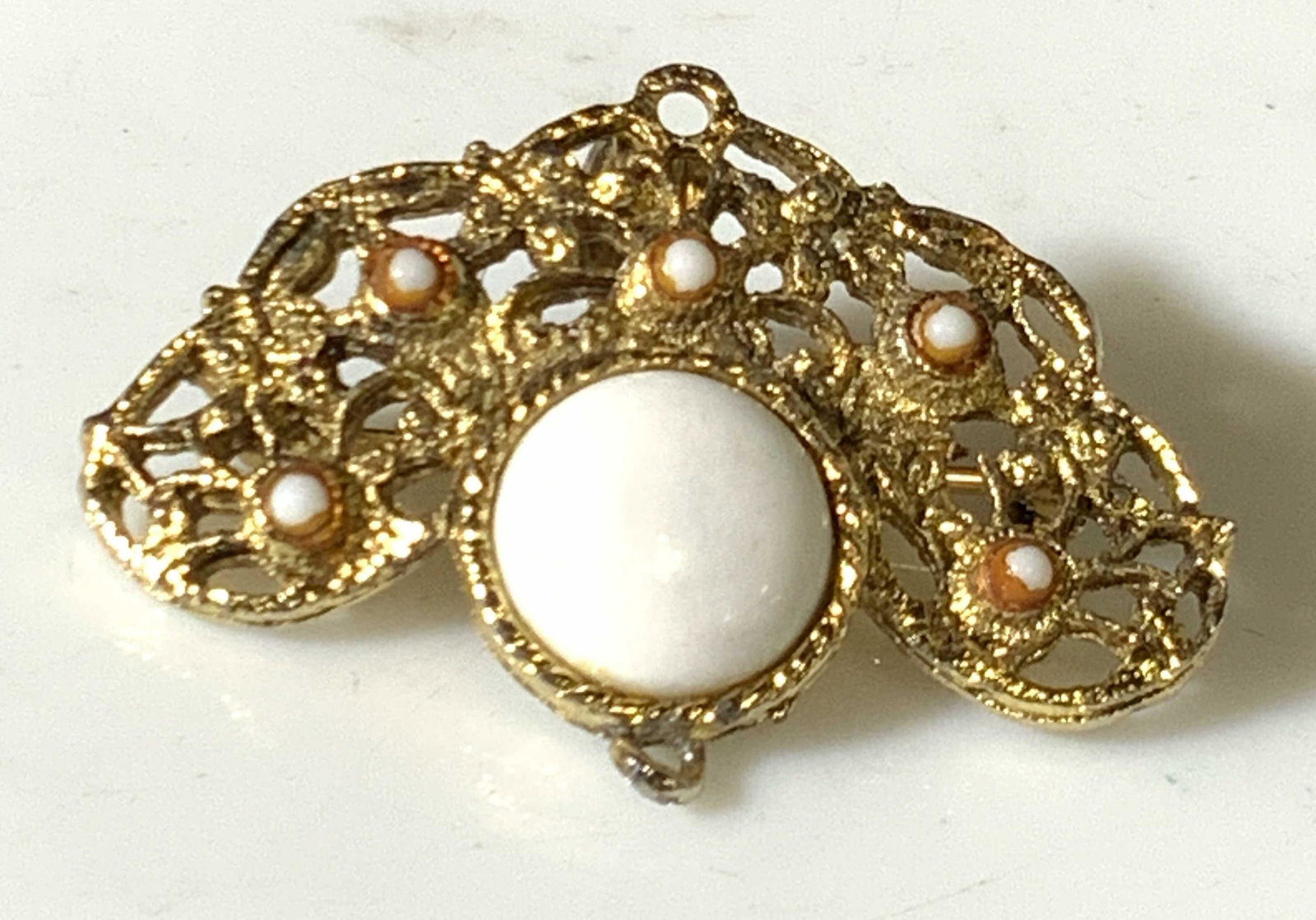 Victorian Style Reticulated Pierced Metal Broach: Multipurpose Victorian style pendant with gold toned filigree. Has pin closure & bail. Bezel set center cabochon white stone and smaller orange/white stones. Approx. 1.5 in. width. Approx. 1 in. lengt