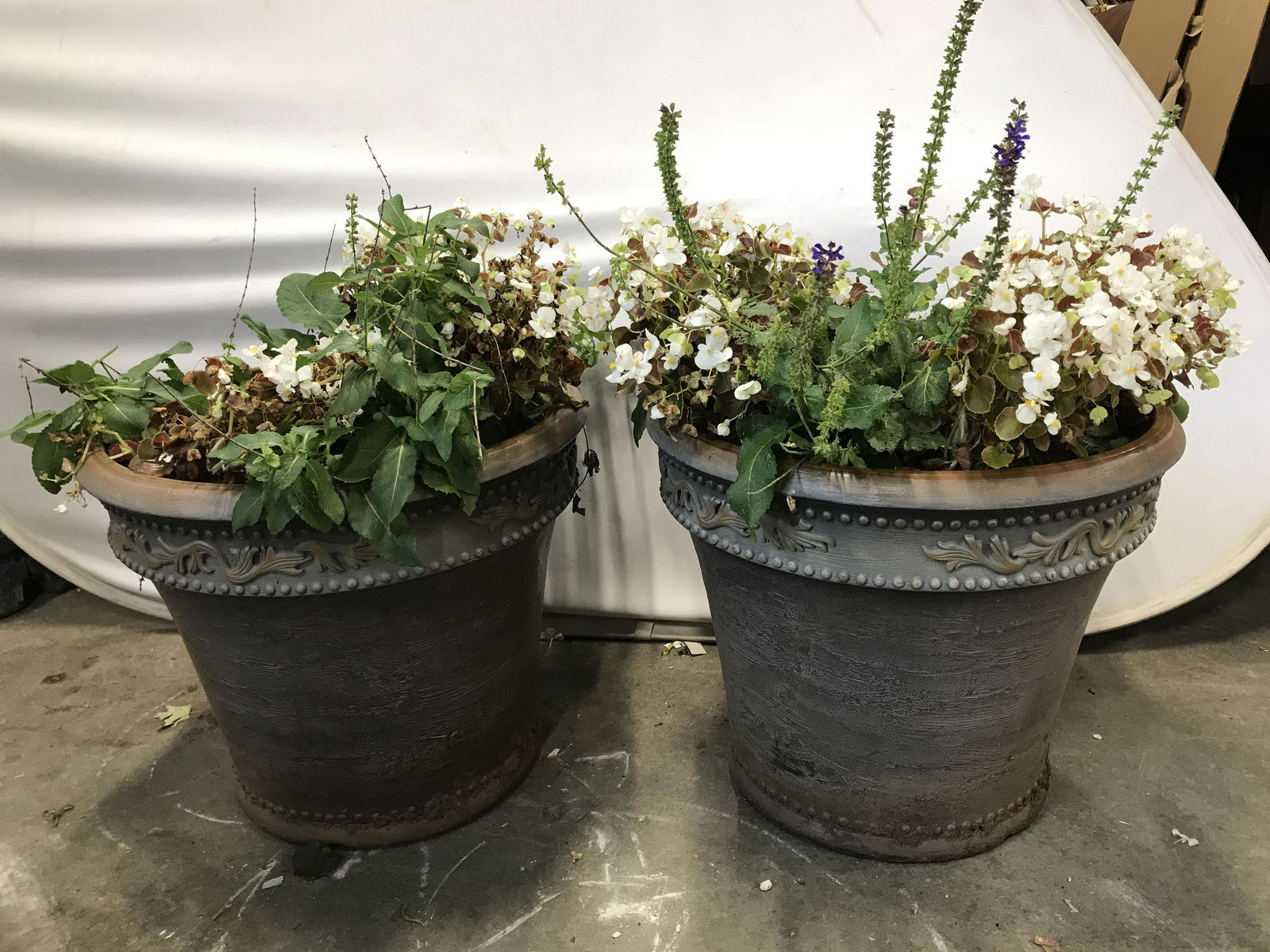 Pair Slate Toned Planters: Lot includes 2 slate toned planters. Each have beveled ornate detail near rim along with stud pattern detail. Planters are possibly composite possibly plastic. Each measures approximately 19 inches ta