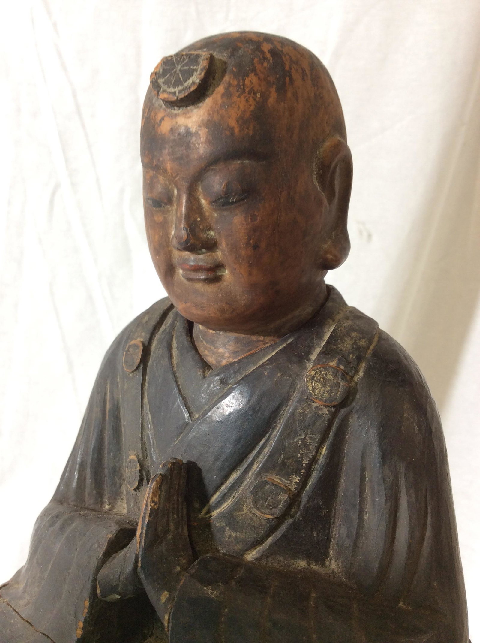 Carved Wooden Buddhist Statue w/ Stand: hand crafted Vintage piece, possibly antique, made of wood, monk sitting on rock in meditative prayer, clothing painted. Wear to wood + fissures/ cracks to piece. App 12 in ht, 6.25 in.W, 5.5 in Depth