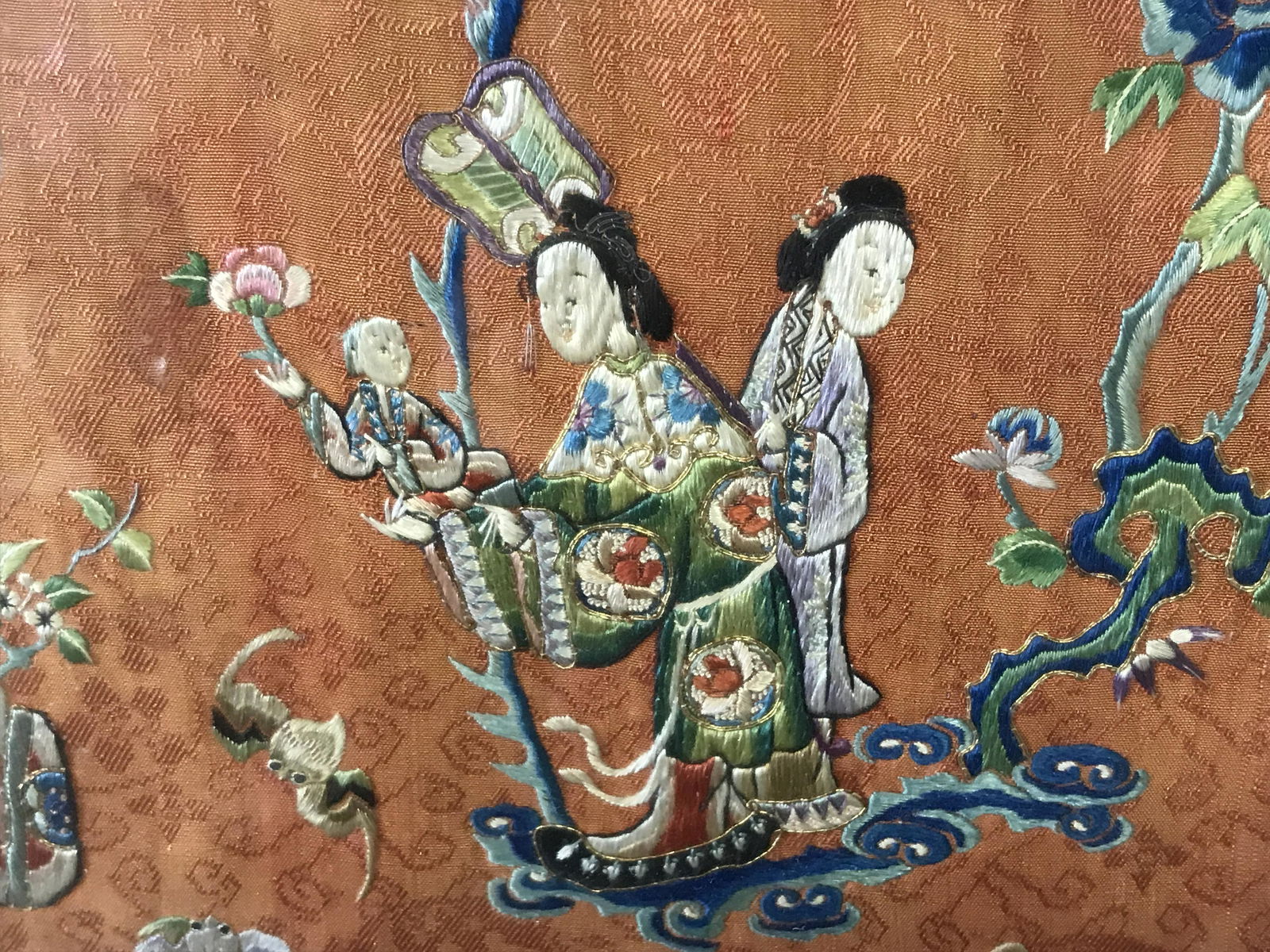 Shadowbox Framed Asian Hand Embroidered Fabric: Framed Asian hand embroidered fabric, no apparent signatures or stamps, subject a blue and orange fabric with a scene of figures in a mystical floral setting, displayed in a shadow box style framing,