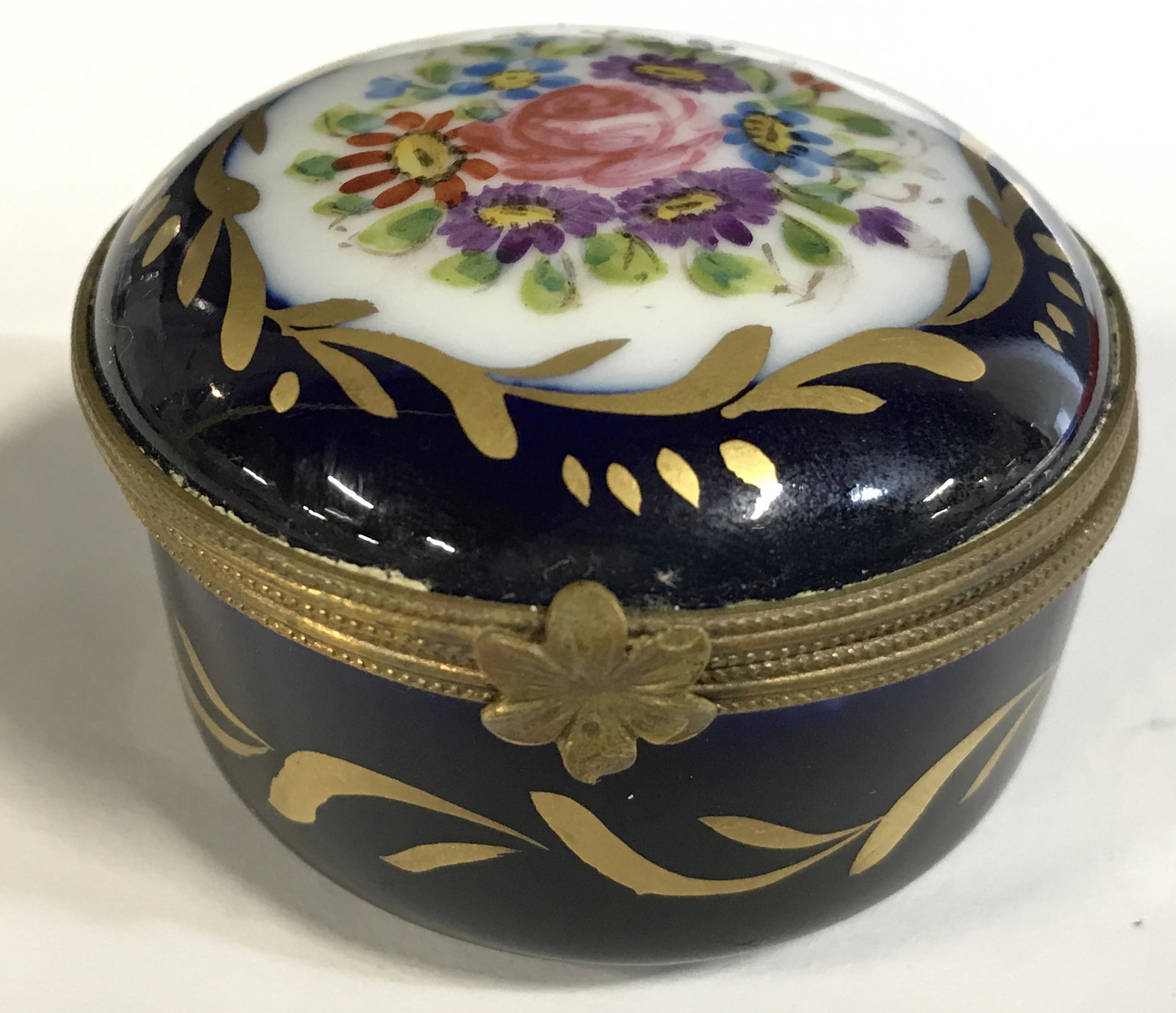 Vintage Porcelain Lidded Trinket / Pill Box: Trinket box is vintage possibly antique. Piece is blue with gold toned accent and multi toned floral and leaf detail. Piece is lidded. Underside is signed and trademarked illegibly. Piece measures app
