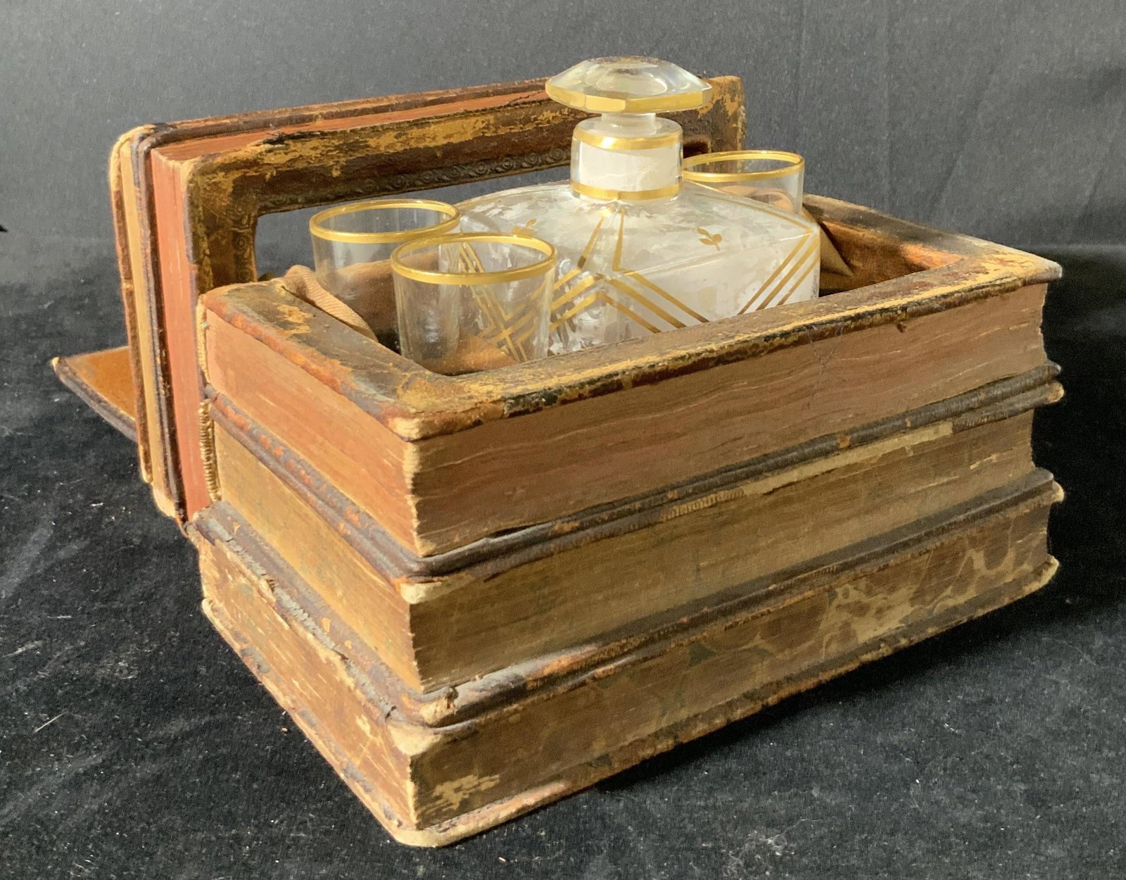 Antique Hidden Bar Stacked Books,19th Century: Antique hidden bar w/ one glass decanter and settings for 4 glass shot glasses, one missing. Glasses & decanter have gilt line work. Decanter has pink shavings in it, possibly a dried beverage. Imitat