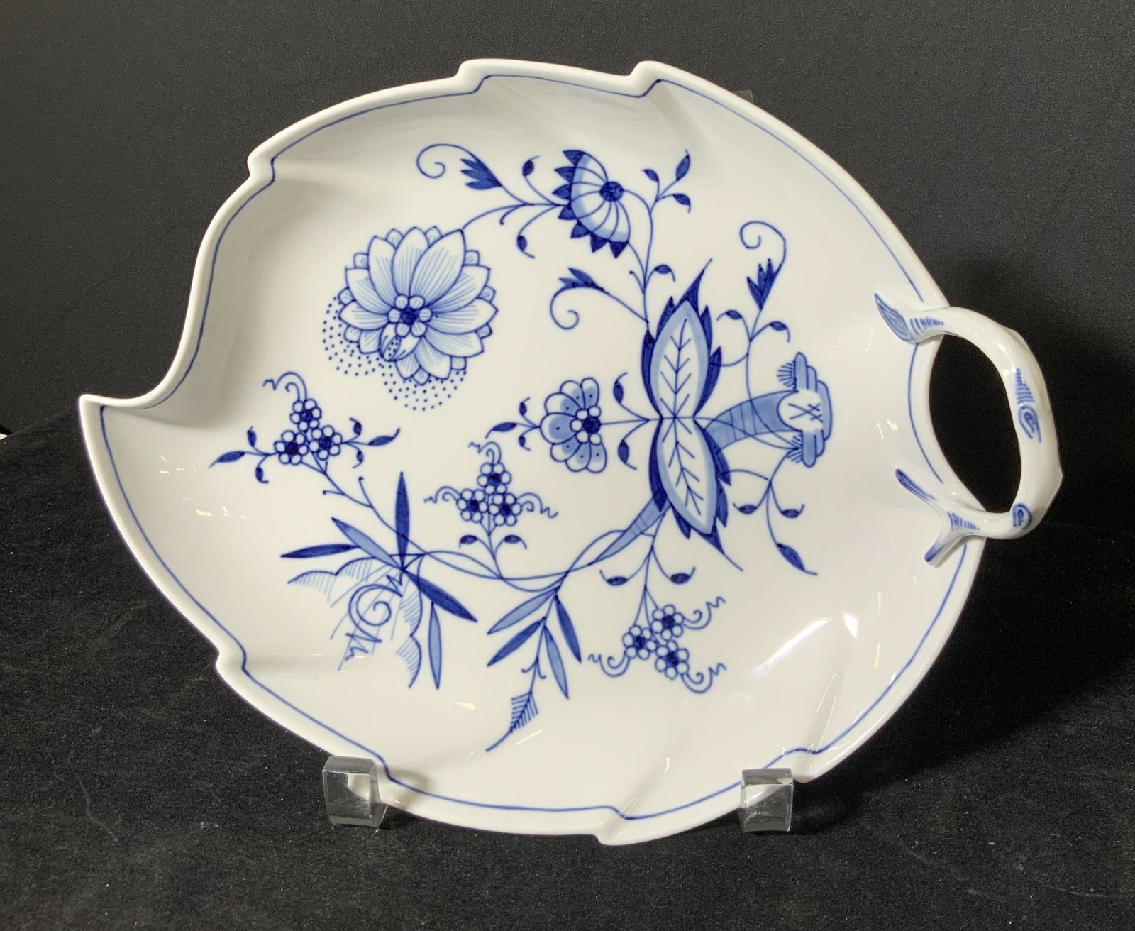 Signed Meissen Blue Onion Cross-Sword Dish: White porcelain with painted cobalt blue floral and leaf designs. Leaf shaped dish. Decorative handle. Underside signed with the crossed swords symbol, MOE, and impressed numbers 266 & 7617. Height ap