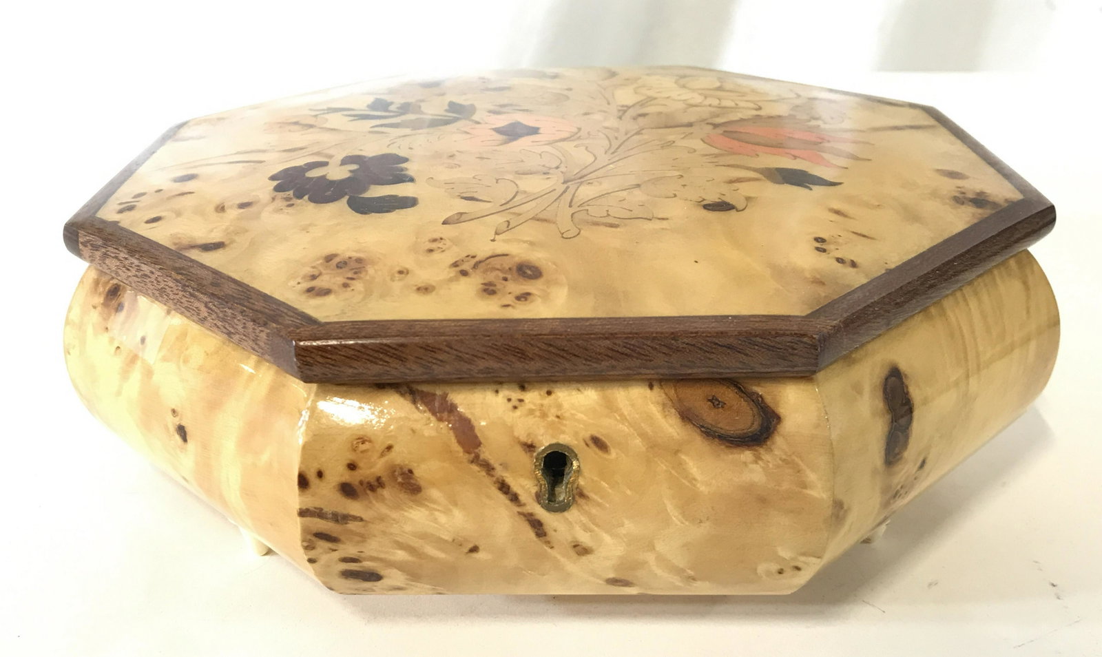 S LUCIA Carved Wooden Music Box: Music box has tag on underside which reads S LUCIA. Piece appears to be wooden, possibly carved bone. Box has octagonal shape. Interior is red toned. Top of lid has multi toned floral and leaf detail.