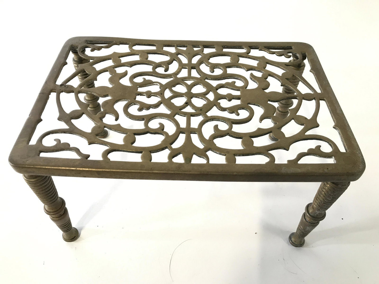 Antique Brass Fireplace Trivet: Fireplace trivet is antique. Piece is gold toned and brass. Piece has pierced detail at top. Measures approximately 9 inches long 6 inches wide 5 inches tall. Trivet, brass trivet, antique trivet, fir