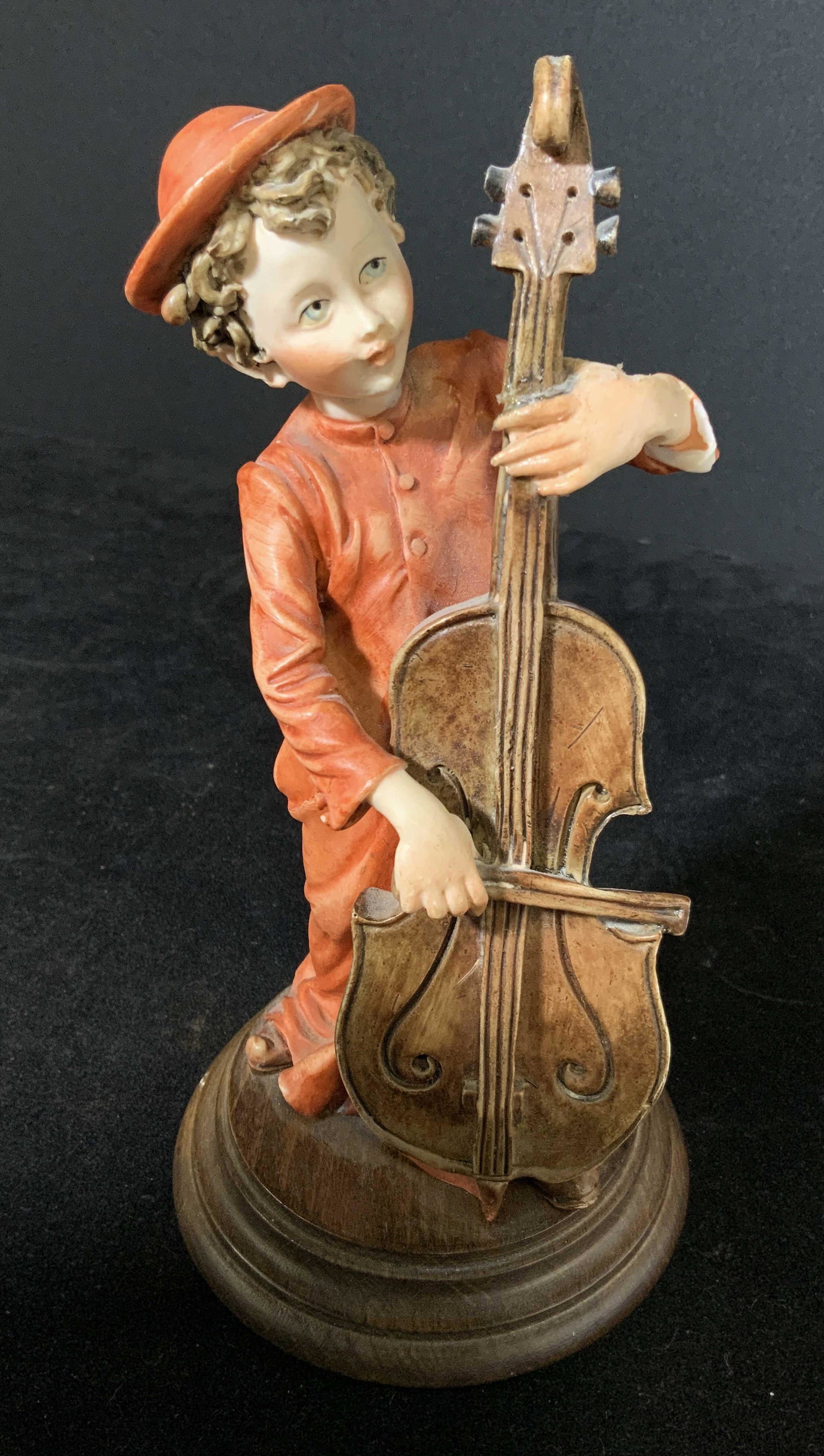 Signed Boy Playing Cello Vintage Figural: Signed Hummel depicting a boy playing a cello. Figural standing on a wooden platform. Figural possibly made by Giuseppe Armani. Bottom of figurals clothing is signed ‘ g.a. ‘ with a symbol beside 