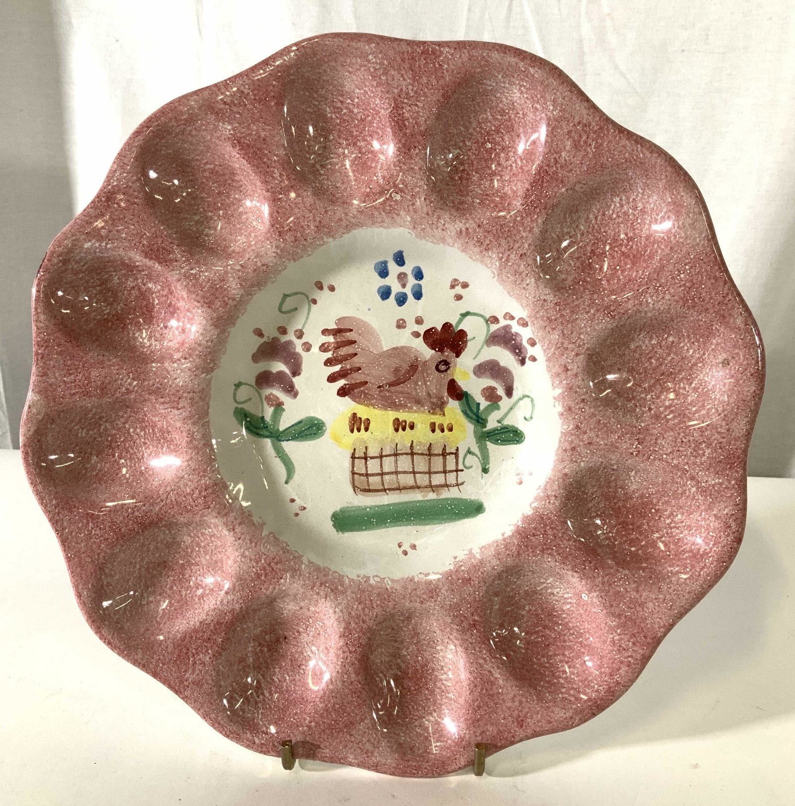 Signed Taste Seller Sigma Ceramic Egg Plate, Italy: Hand decorative egg display plate, Center decor depicts chicken laying eggs whilst sitting in a basket. Spotted Pinkish- red Border paint on white porcelain. App 11.5 in. Reverse side with label Telle