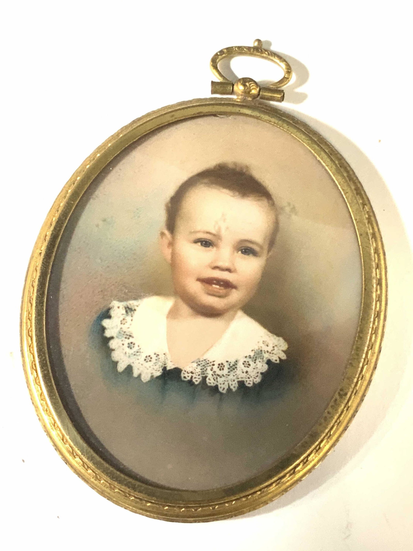 Victorian Metal Gold Toned Portrait Pendant: Large pendant with the portrait of a toddler in the center. Polished gold toned metal. Decorative impressed metal bail and backing. Clear covering over portrait. Pendant Approx. 3.5 in. height. Approx