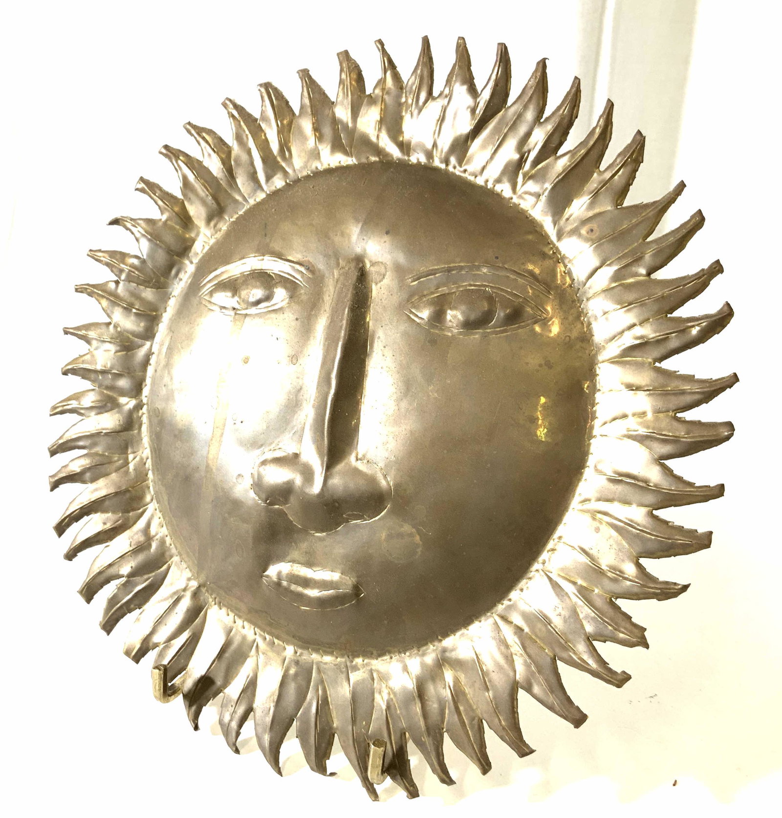 Hand Crafted Brass tnd Sunburst Ornament Sri Lanka: Repoussé Sun with face, made by hand in Sri Lanka ( sticker on verso). Attached brass piece to hang on wall. Each sun ray hand cut with reticulated sun ray pattern. Large primitive facial features. 9