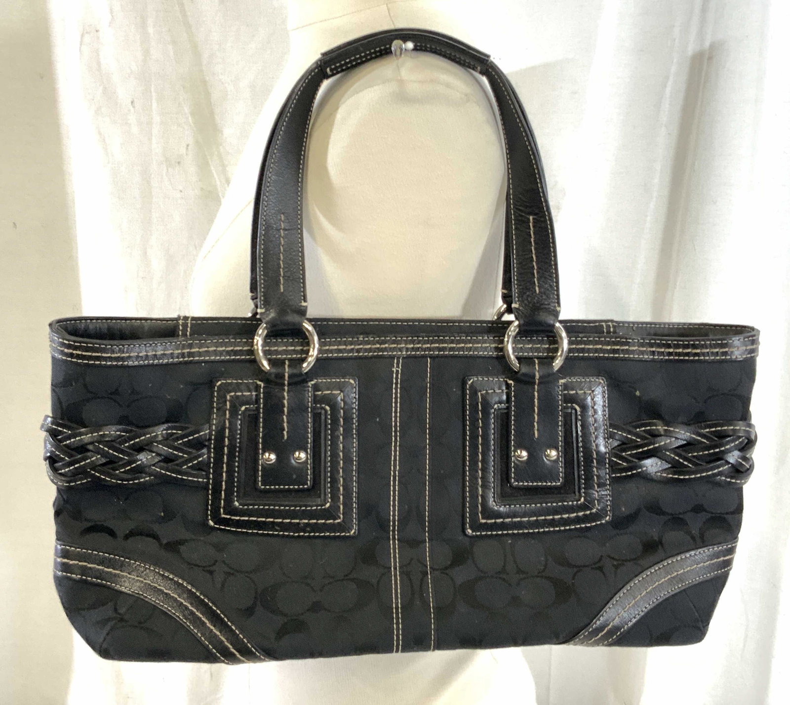 Large Soho Black COACH Braided Satchel Purse: Large COACH black fabric with iconic signature ‘ C ‘ design. Made with leather. Accented with white contrasting stitching and black braided leather buckle accent. COACH embossed tag on strap. Silv