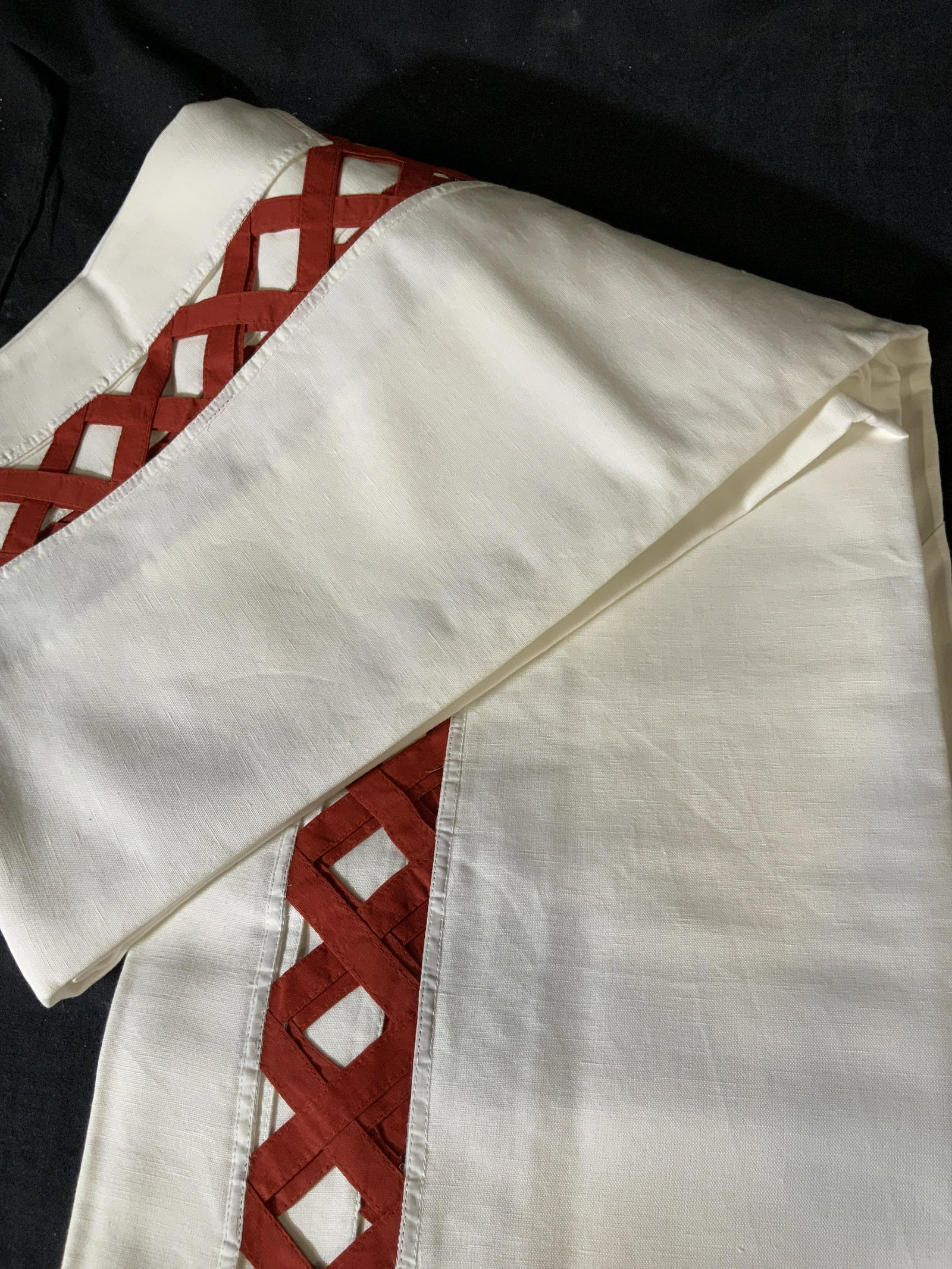 Set of Two Decorative Tablecloths: Set of two large table clothes in white with a red peek-a-boo basket pattern around the edge of the table where it hangs over the side of the table, made of linen the basket pattern is in a chili red,