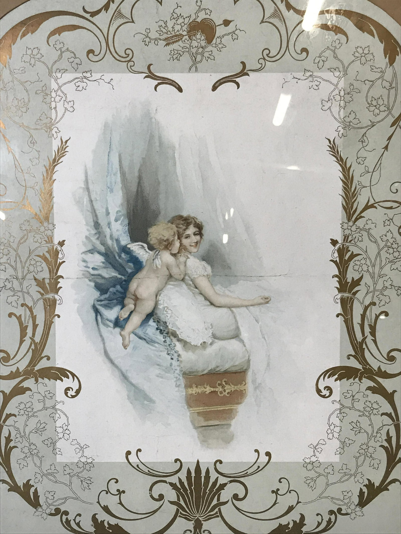 Rococo Style Lithograph ‘Whispers of Love’: Rococo style lithograph, title along the lower center border reads ‘Whispers of Love’, subject a woman lying in bed with a Cupid or a putti at her shoulder, gold floral accents surround the piece,