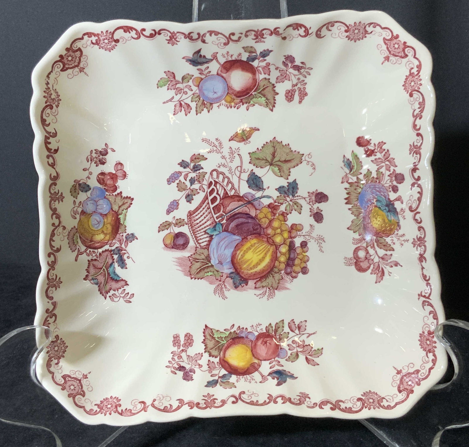 Signed MASON’S Ironstone ‘Fruit Basket’ Dish: Signed square ironstone dish with fruit and fruit basket motif throughout. Scalloped edges. Colors include burgundy, yellows, blues, and greens. Various fruits depicted; grapes, berries, and more. Und