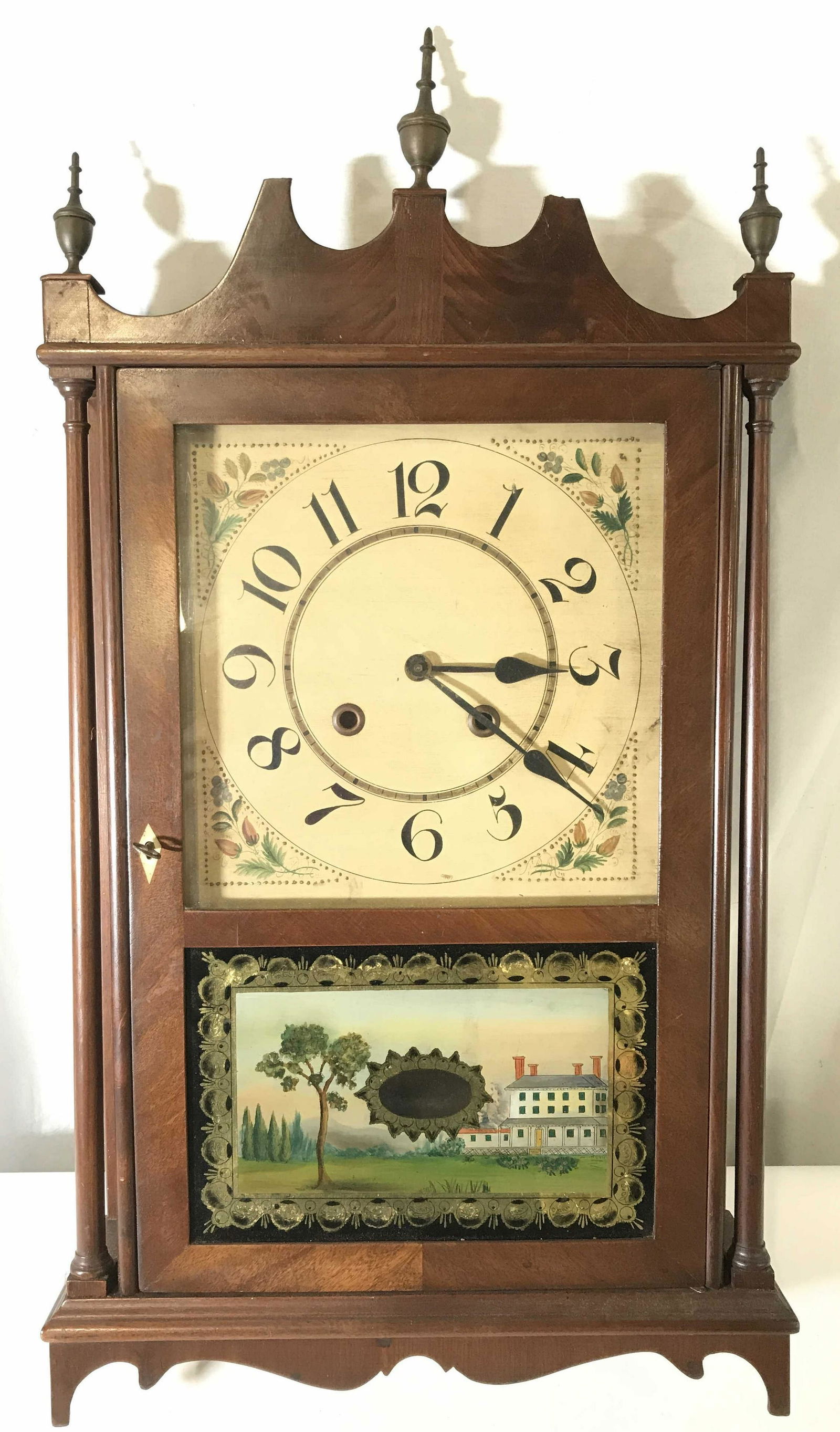Vintage Wall Clock W Hand Painted Glass: Vintage, possibly antique, wall clock. Pendulum window is hand painted and depicts a house among trees, window border is gold toned. Clock face is wooden, and hand painted, three brass finials adorn c