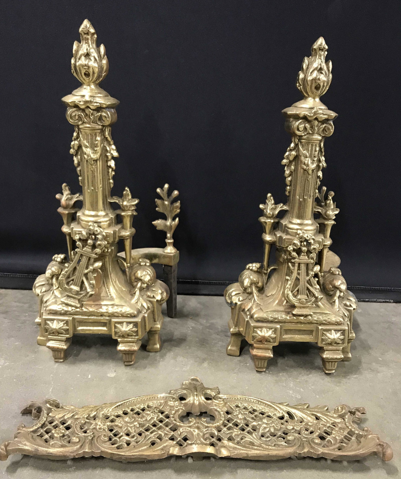 Vintage Set 3 Piece Brass Fire Place Accessories: Fireplace set is gold toned and brass. Lot includes 2 andirons and 1openwork plaque. Each piece has intricate ornate detail. Andirons measure approx 17 inches tall 8 inches wide 7 inches deep. Firepla