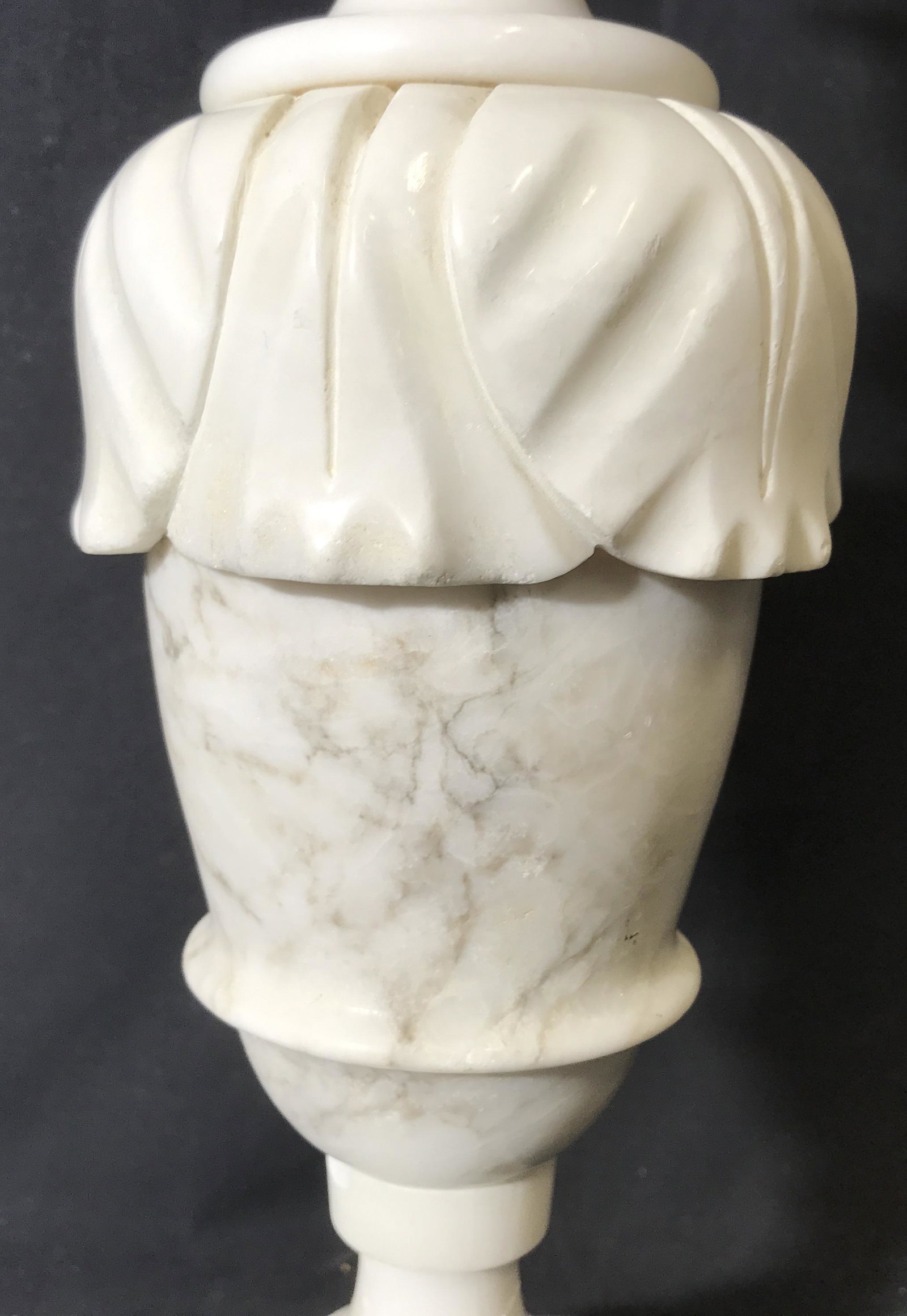 White Marble Urn Style Table Lamp: White marble lamp, felt bottom to lamp, body of the lamp shaped like a vase with acanthus leaves, single bulb lamp, broken gold toned metal harp, some chips to marble, base measures as a 4.75 inch squ