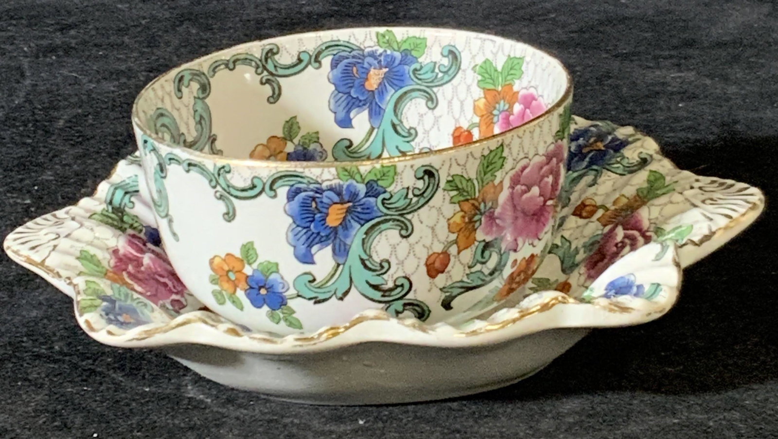 Set 2 BOOTHS Signed Antique Floradora Cup & Saucer: Antique cup and saucer set (2) with decorative floral motifs throughout. Colors include pinks, blues, oranges, and gilt line work. Saucer has scalloped edges and embossed ruffling. Undersides read: BO