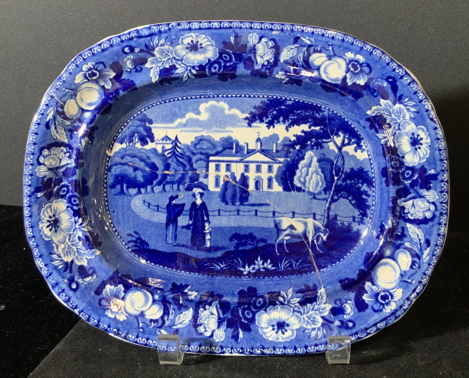 BRITISH VIEWS Signed Antique Collectible Plate: Blue and white collectible porcelain plate. Elongated oval with slight scalloped rim. Scene depicts people, cow, buildings, and floral motifs. Underside trademarked with floral / vine motif, reads: BR