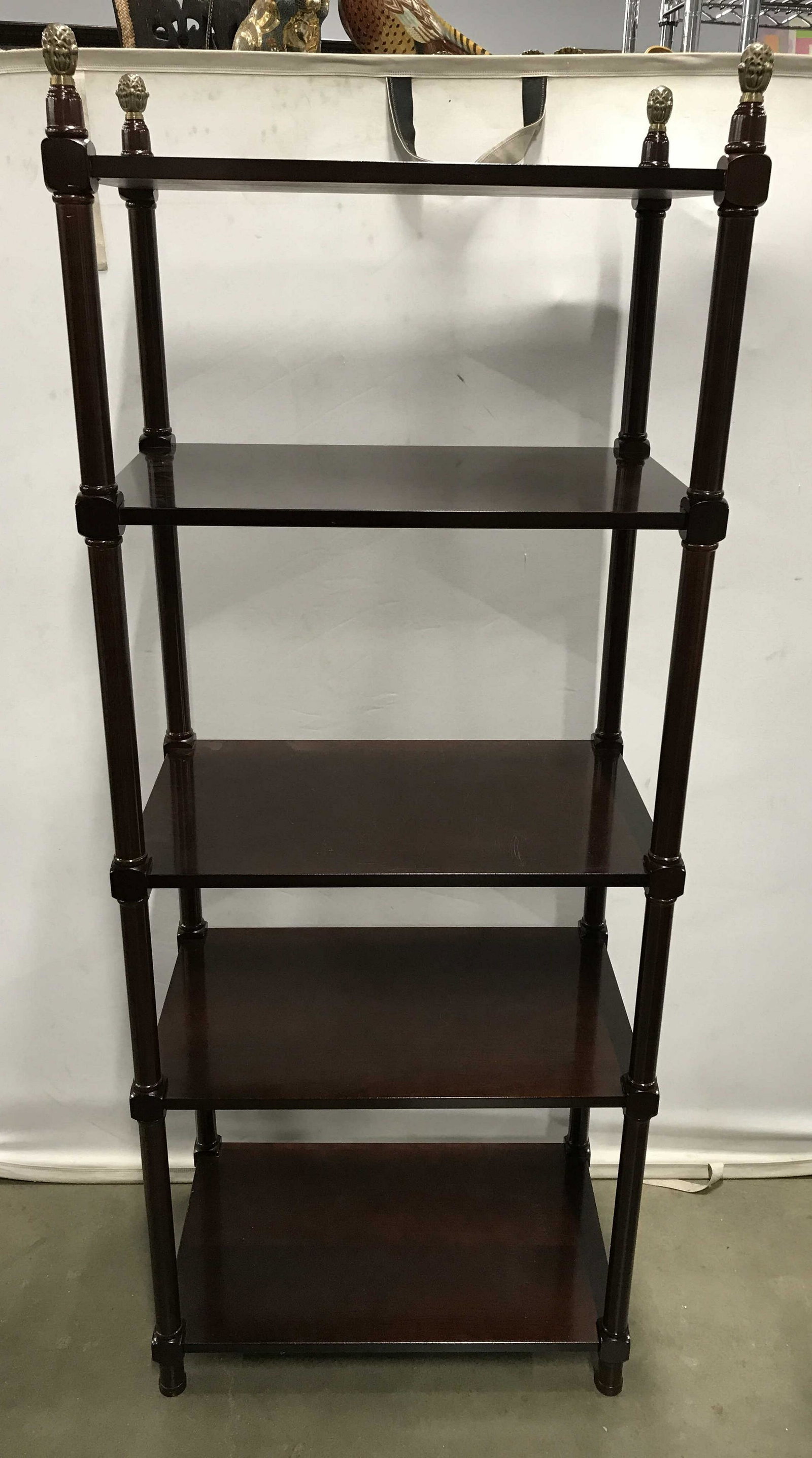 THE BOMBAY COMPANY Walnut Toned Shelves: Walnut toned shelves, possibly vintage. Each corner of the shelves are topped with a brass finial. Measures approx 66.75 inches H, 26.25 inches W, and 16.25 inches deep. Label on underside reads as TH