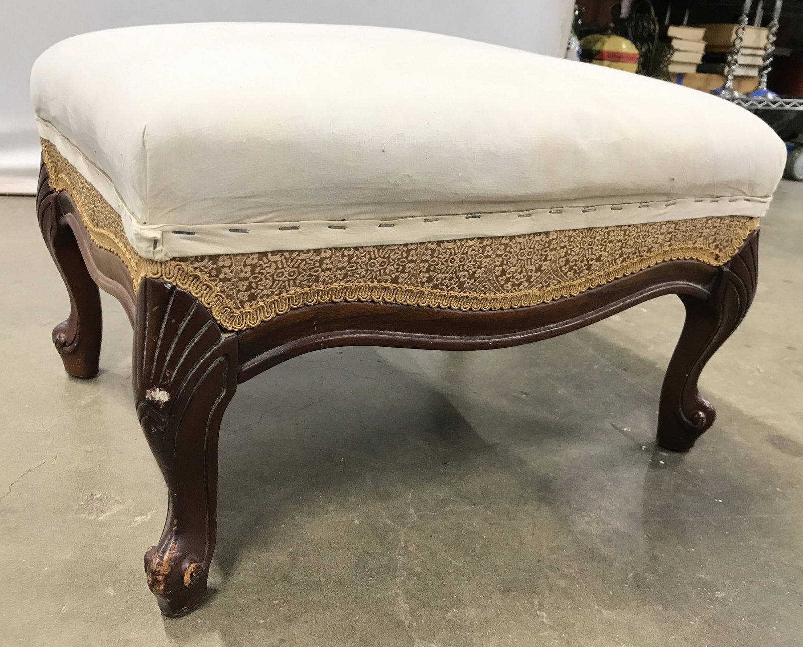 Antique Upholstered Footstool: Footstool is antique. Piece is upholstered with cream toned fabric. Footstool has carved wooden feet. Piece has intricately detail upholstery near wooden area. Piece measures approximately 21 inches l