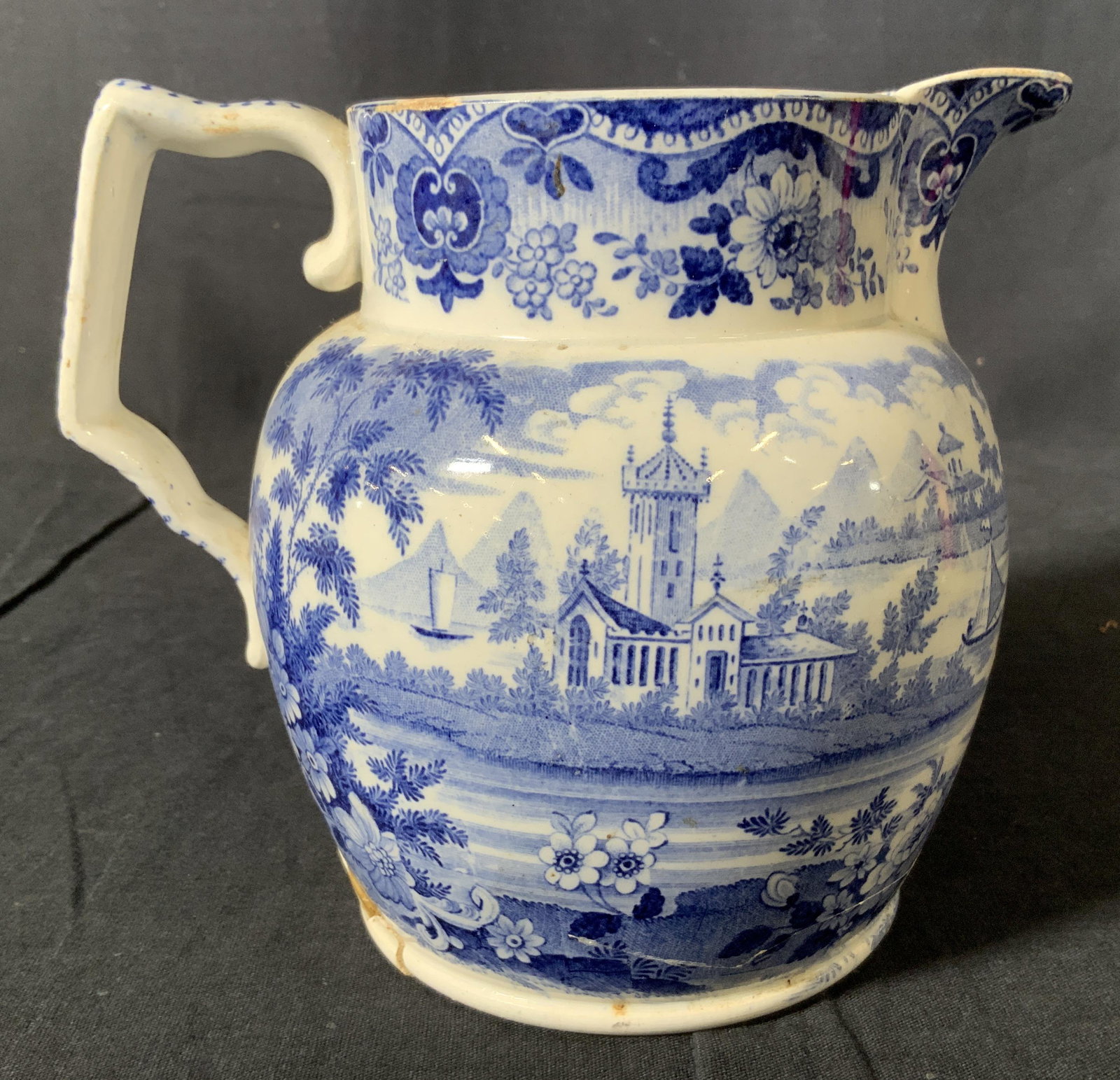 Antique Blue & White Ceramic Pitcher: Antique Blue & White Ceramic Pitcher, no apparent inscriptions or stamps, design features houses in the midst of a lake, measures 5 7/8 x 6 3/4 inches at widest point, Cracks to base repaired, some mi