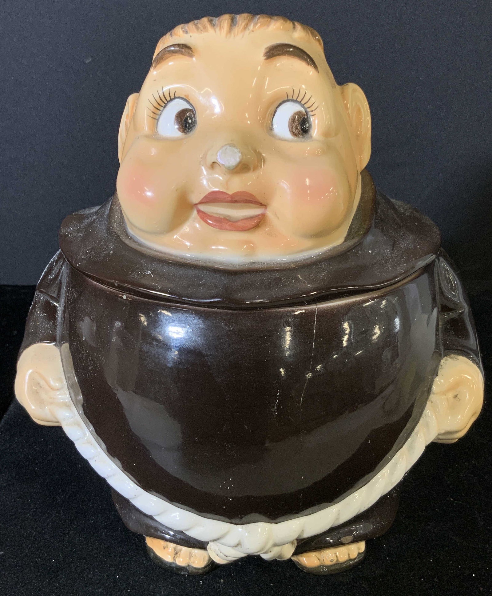 Vintage Monk Figural Ceramic Lidded Cookie Jar: Lidded ceramic cookie jar shaped like a monk / friar. He has brown hair, brown eyes, and smiling mauve lips. Head is lid, body is jar. He wears classic brown robes with white rope sash. Surface wear o