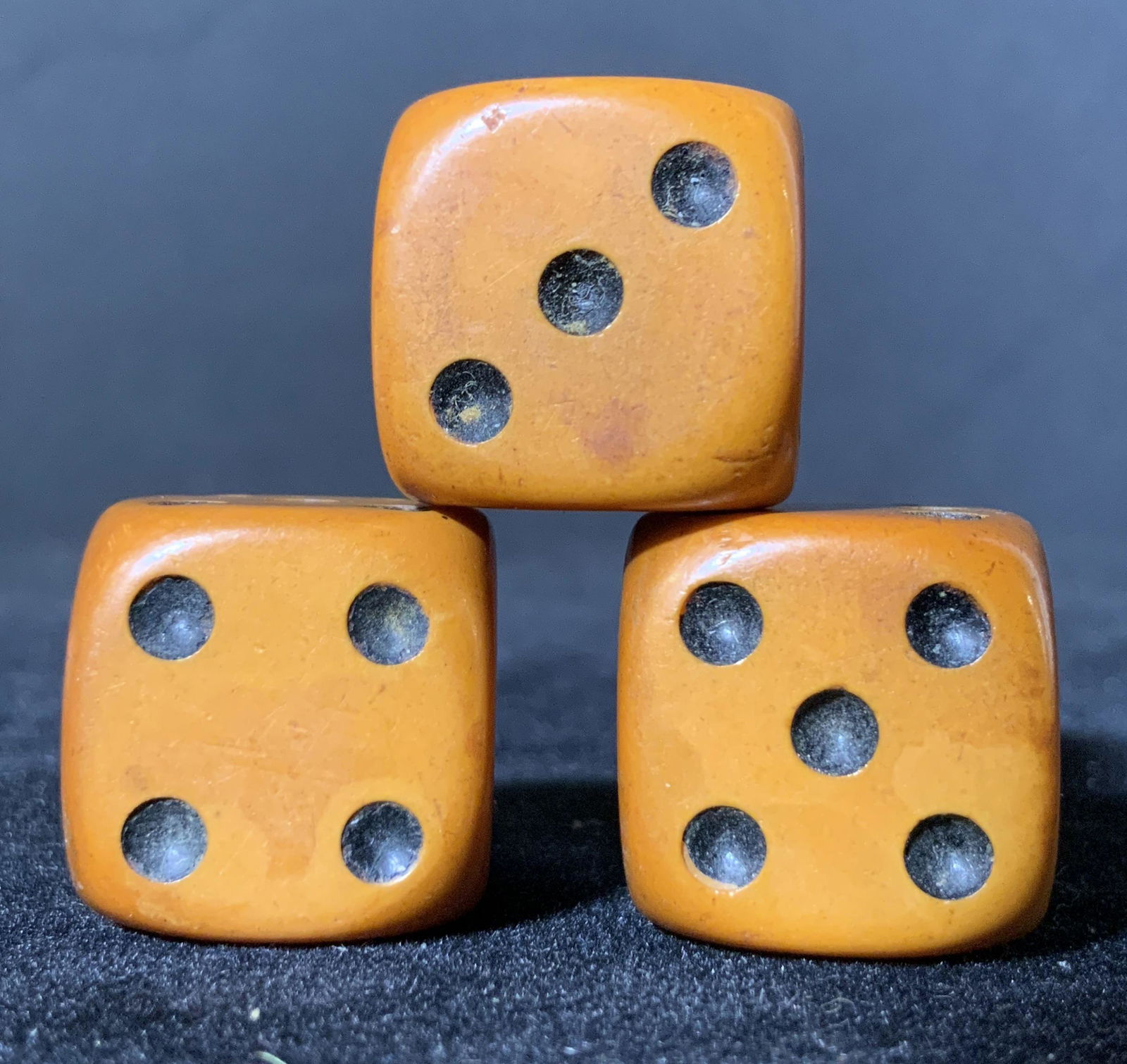 Set 3 Collectible Antique Bakelite Brown Dice: 3 dice, possibly Bakelite, that are brown in color. Black indents indicating numbers on each side of dice. Dice are a bit more rounded on the edges. Some wear to the black coloring. Approx. .5 x .5 in
