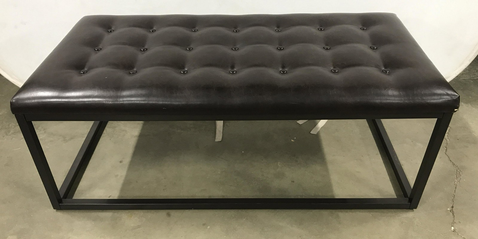 PERMAISURI CO LTD. Tufted Leather Metal Bench: Button tufted leather bench, the frame is metal, colored black. The piece measures approx 17.5 inches H, 47.5 inches W, and 23.5 inches deep. Wear present is consistent with use, a small hole is prese