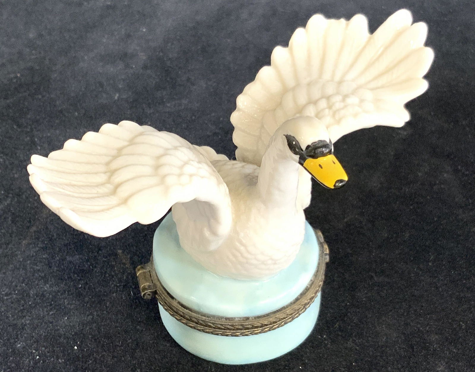 Porcelain Swan Figural Hinged Pill Box: A porcelain swan about to take flight atop a light blue porcelain pill box. The swan has embossed pottery feathers. The bill is yellow with black accents. The porcelain pill box has etched metal hardw
