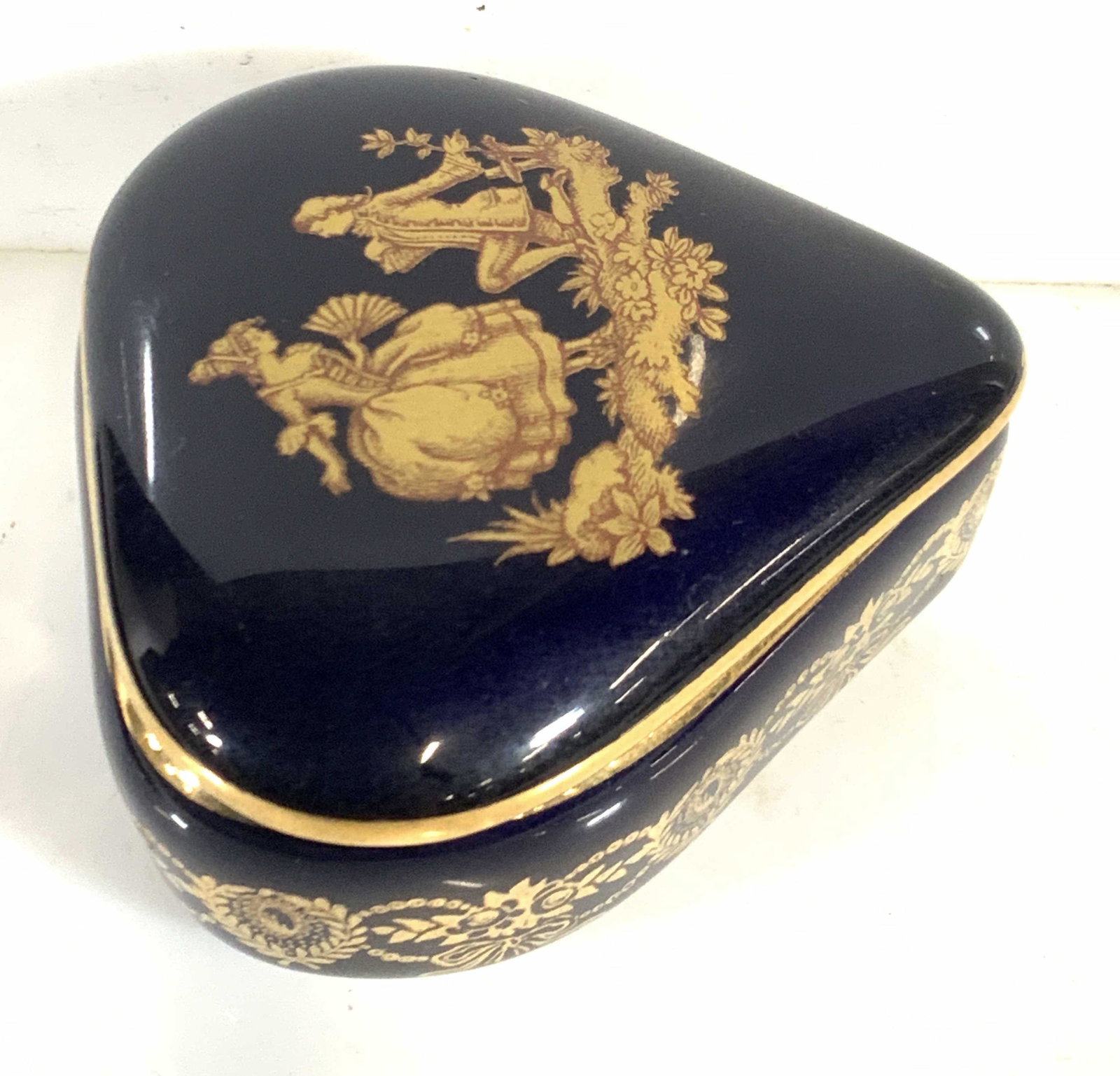 LIMOGES Signed French Deep Blue Triangle Pill Box: Deep blue triangular shaped porcelain lidded pill box with two characters depicted on the lid. Gilt line work throughout. Interior trimming white porcelain, interior overall blue. Underside trademarke