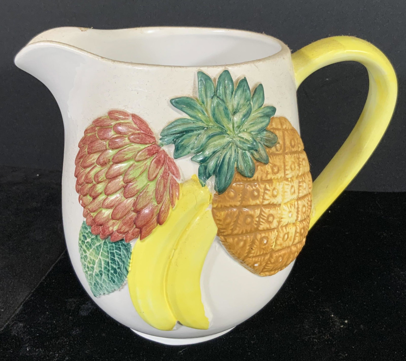 BASSANO Sig. Vintage Majolica Fruit Pitcher, Italy: White ceramic pitcher with a yellow handle and Majolica fruit on the front side. The depicted fruits are pineapple, banana, and a berry with a leaf. The underside is trademarked and signed: BASSANO It