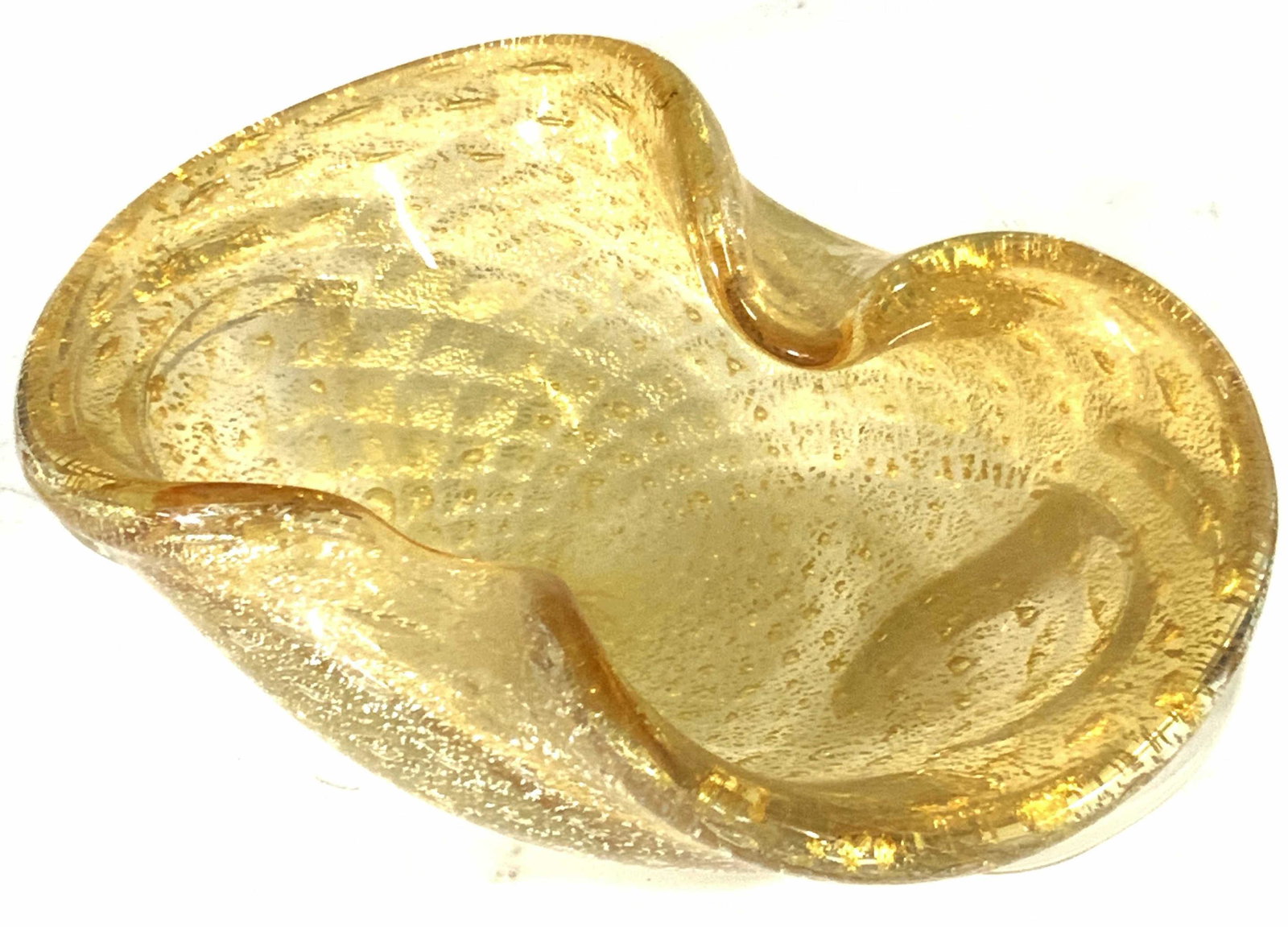 Abstract Artisan Gold Fleck Art Glass Trinket Dish: A uniquely shaped trinket dish with two underside handles. Center of underside is flat and smooth. Gold flecks throughout thick walled clear glass. Approx. Height 2.25 in. Approx. Width 6.5 in. Art gl