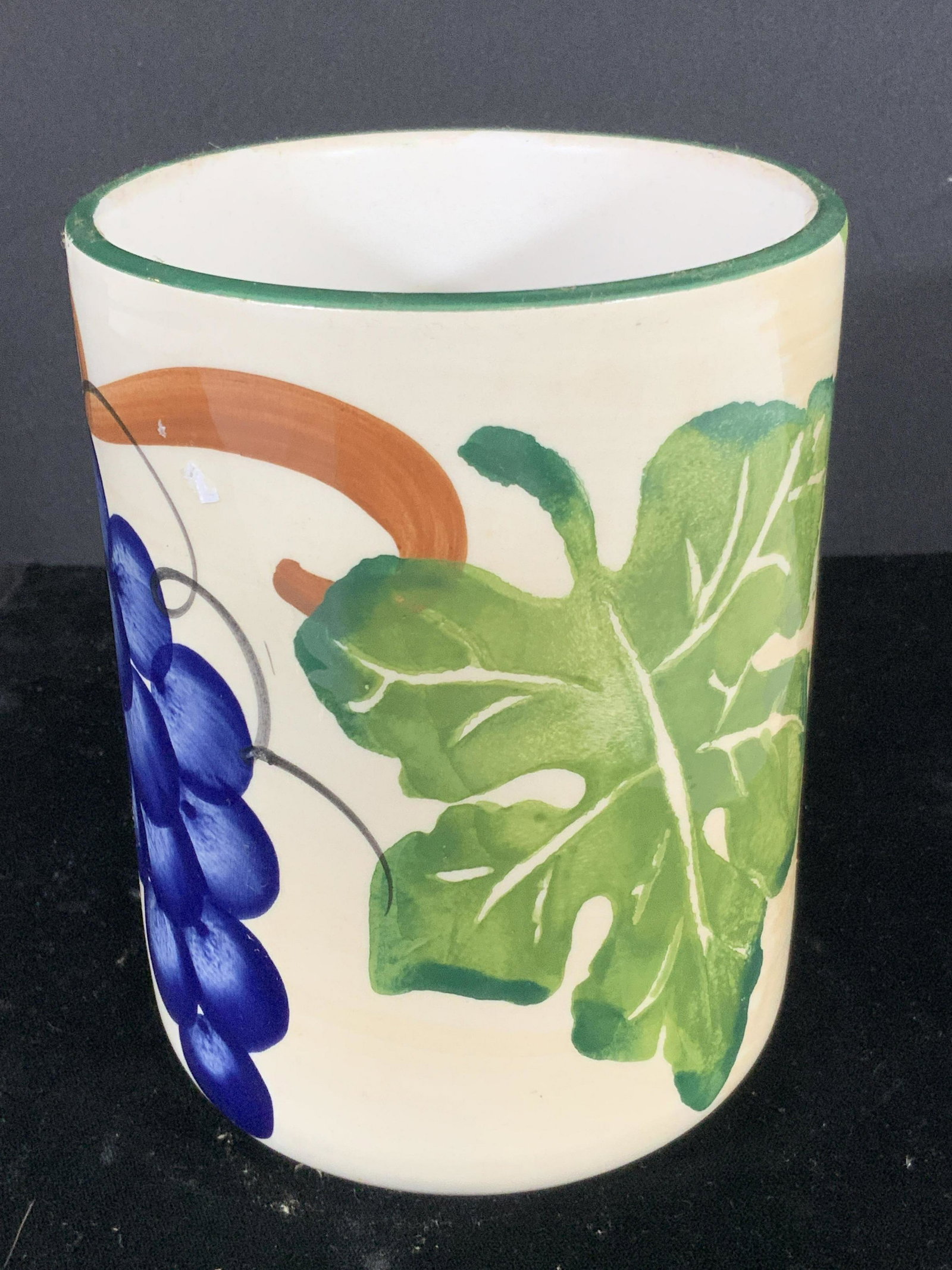 Italian Hand Painted Ceramic Cylindrical Vase: Designs on this vase feature grapes, cherries, leaves, and vines. Cylindrical vase is mostly white. Colors include greens, browns, blues, and reds. Underside reads: Made in Italy. Approx. Height 6 in.