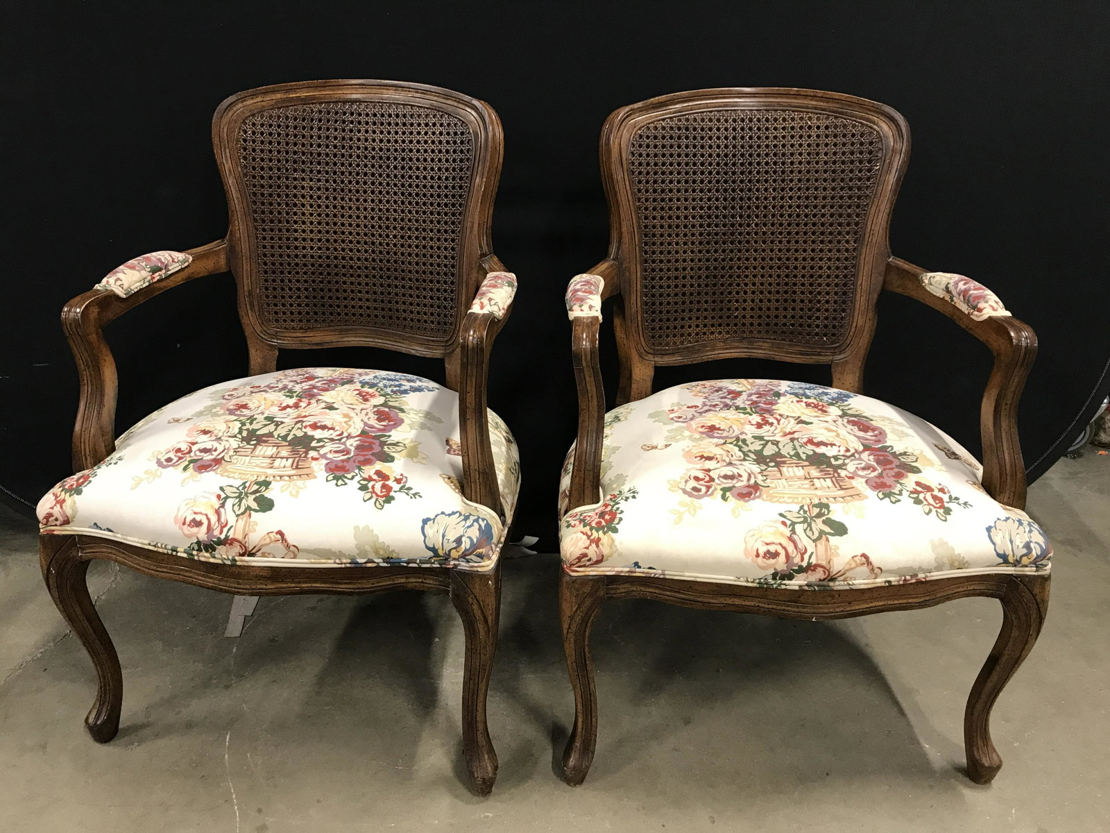Pair Bergere Arm Chairs: Pair of Bergere arm chairs, possibly vintage, possibly antique. Upholstery is cream toned, decorated by a multi toned pattern depicting a floral bouquet. Upholstery is double welted, back appears to b
