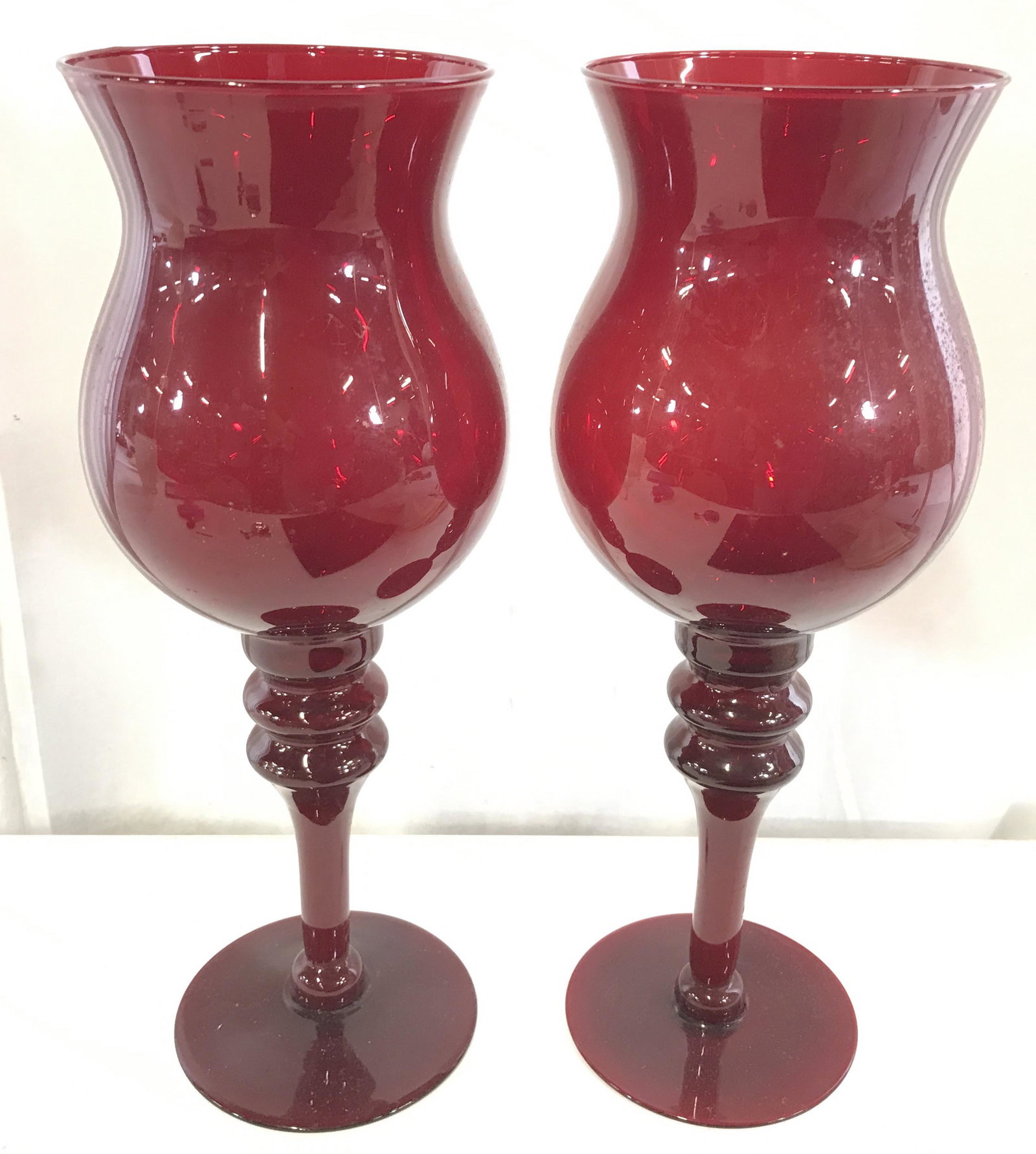 Pair Ruby Red Art Glass Candle Holders: Pair of cherry toned Glass candle holder. Each resembles a chalice. Measure approx 14.5 inches H, and 5.5 inches W. Wear is consistent with age and use. Vintage decor, art glass, candle holders, vesse