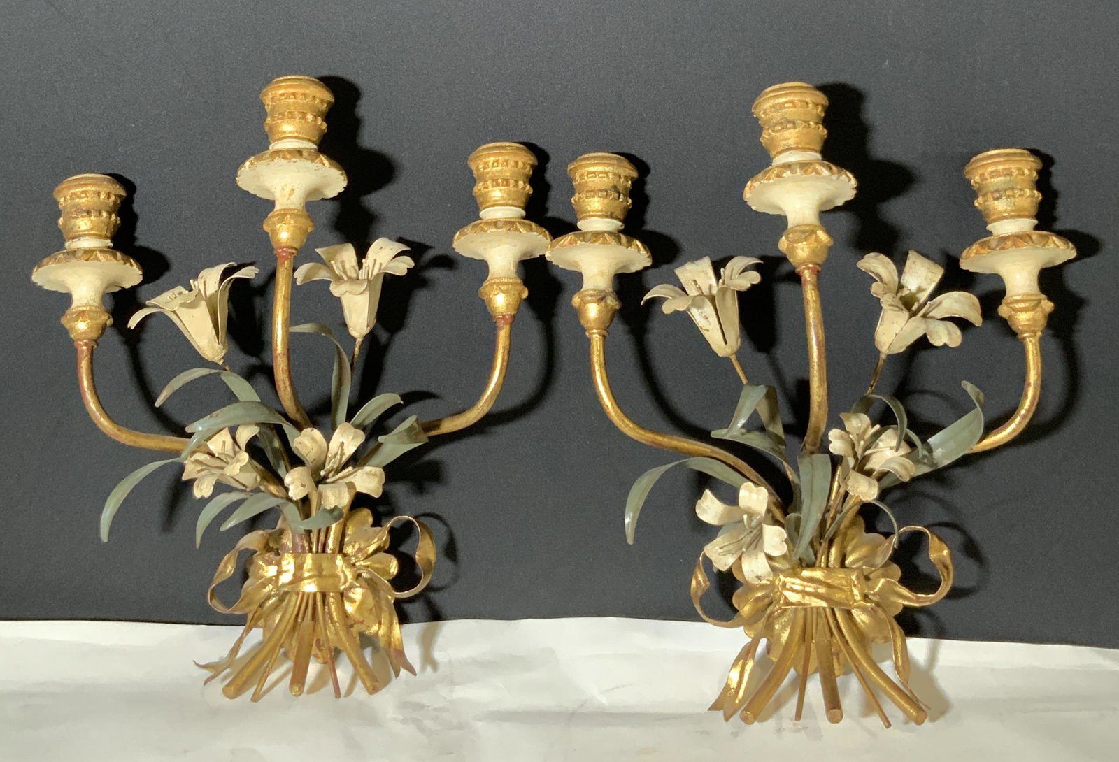 Pair Antique Gilt Metal Tole Wall Sconces, Italy: Metal wall sconces painted with gilt. 3 settings on each for candles. Painted green and white metal flowers and leaves. Underside has metal ring attached that reads: Made in Italy. Approx. 15 in. heig