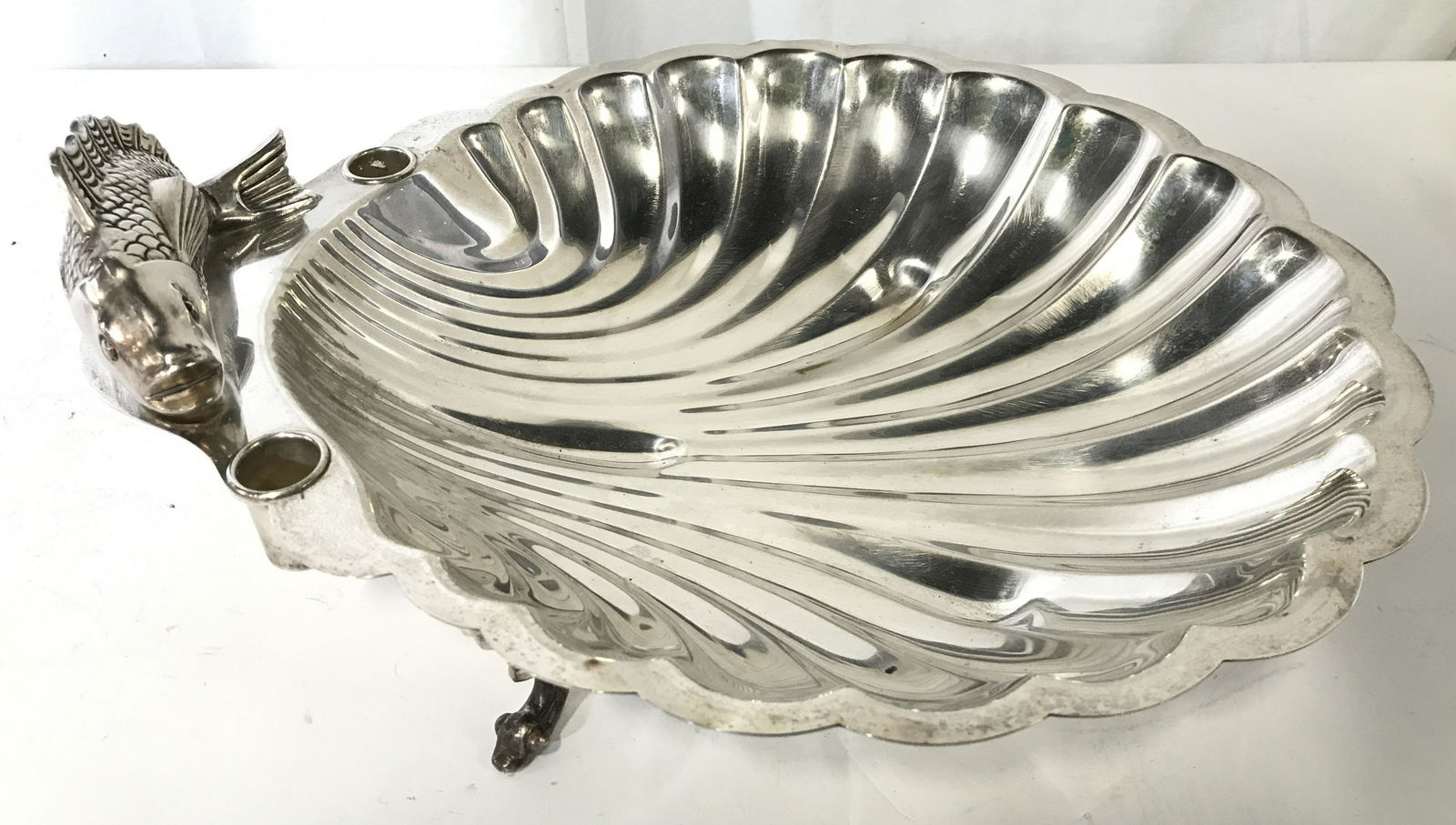 Footed Silver Plated Shell Platter: Underside of piece is marked SILVER PLATED. Piece is footed with 3 feet. One edge of piece has fish Figural. Piece measures approximately 16 inches long 13.5 inches wide 5 inches tall. Shell platter,