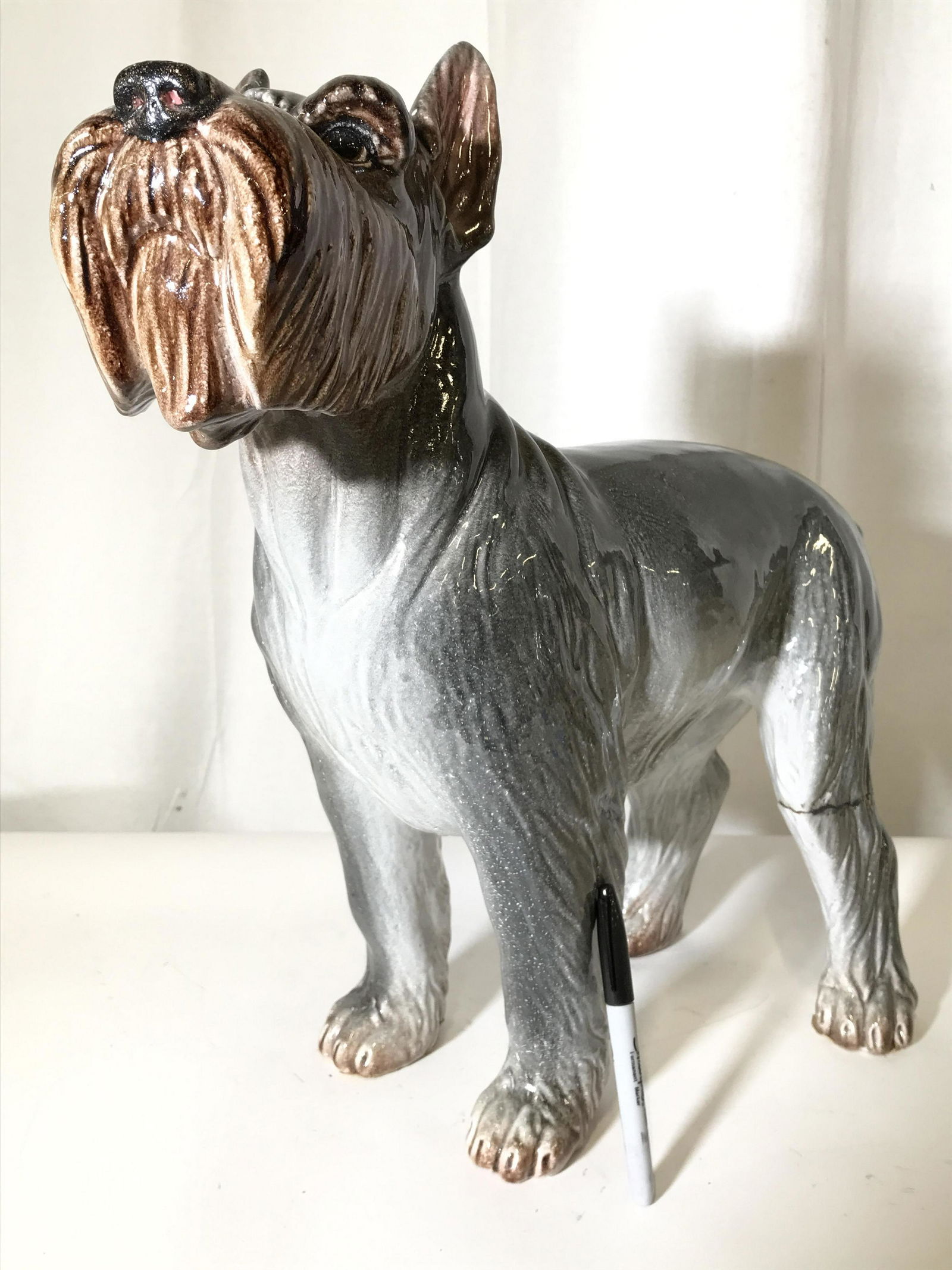 Vintage Large Size Porcelain Schnauzer: Statue is large in size. Piece is porcelain. Statue depicts a grey toned schnauzer with grey and brown toned face. Piece measures approximately 19 inches tall 20 inches long 7 inches wide. Dog statue,