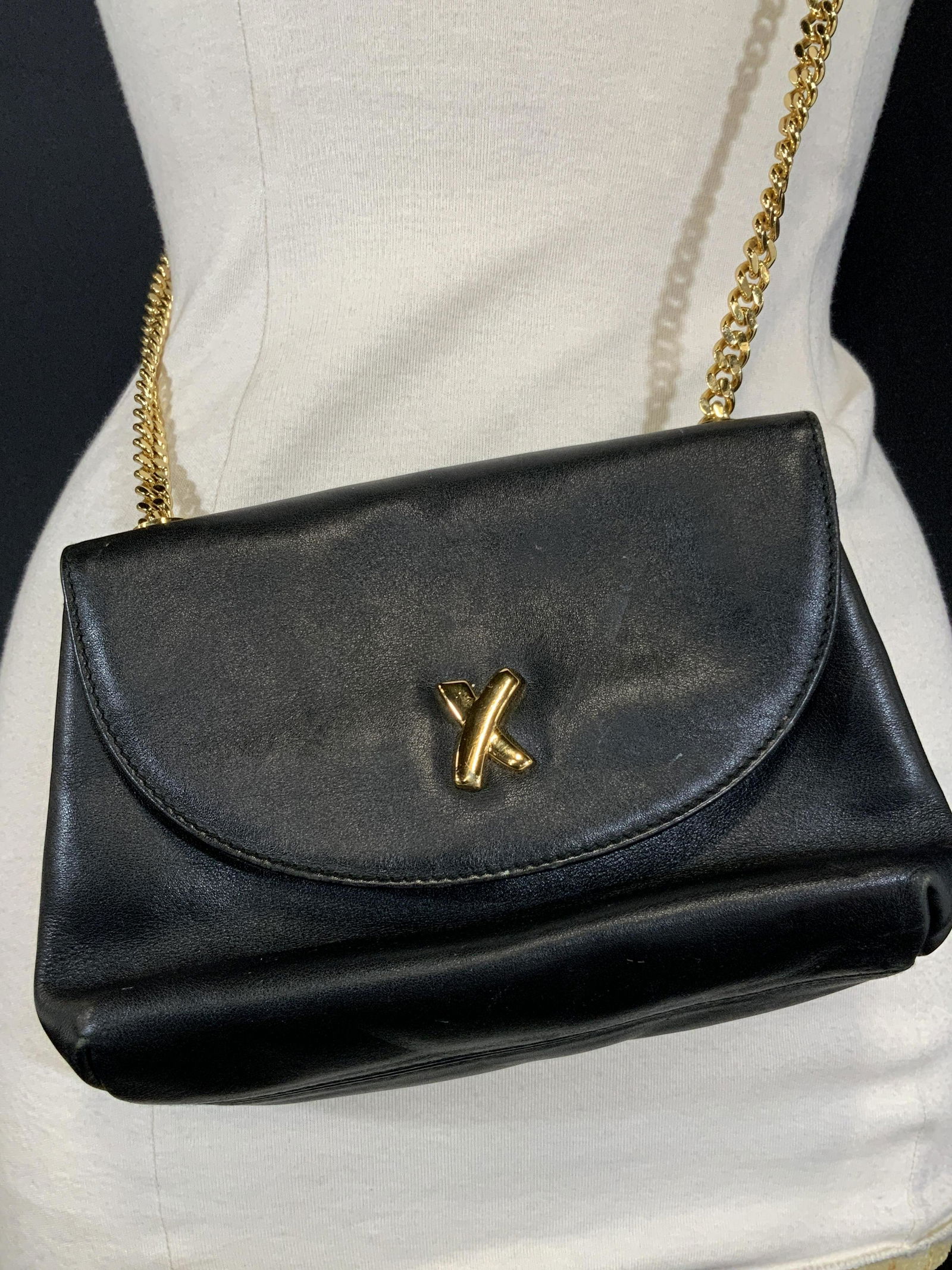PALOMA PICASSO Black Leather Vintage Purse, Italy: Black leather Paloma Picasso Purse w/ gold toned hardware and accents. Snap button closure. Gold toned chain style strap. Interior stitched with black lining reading ‘ Paloma Picasso ‘. 1 interior