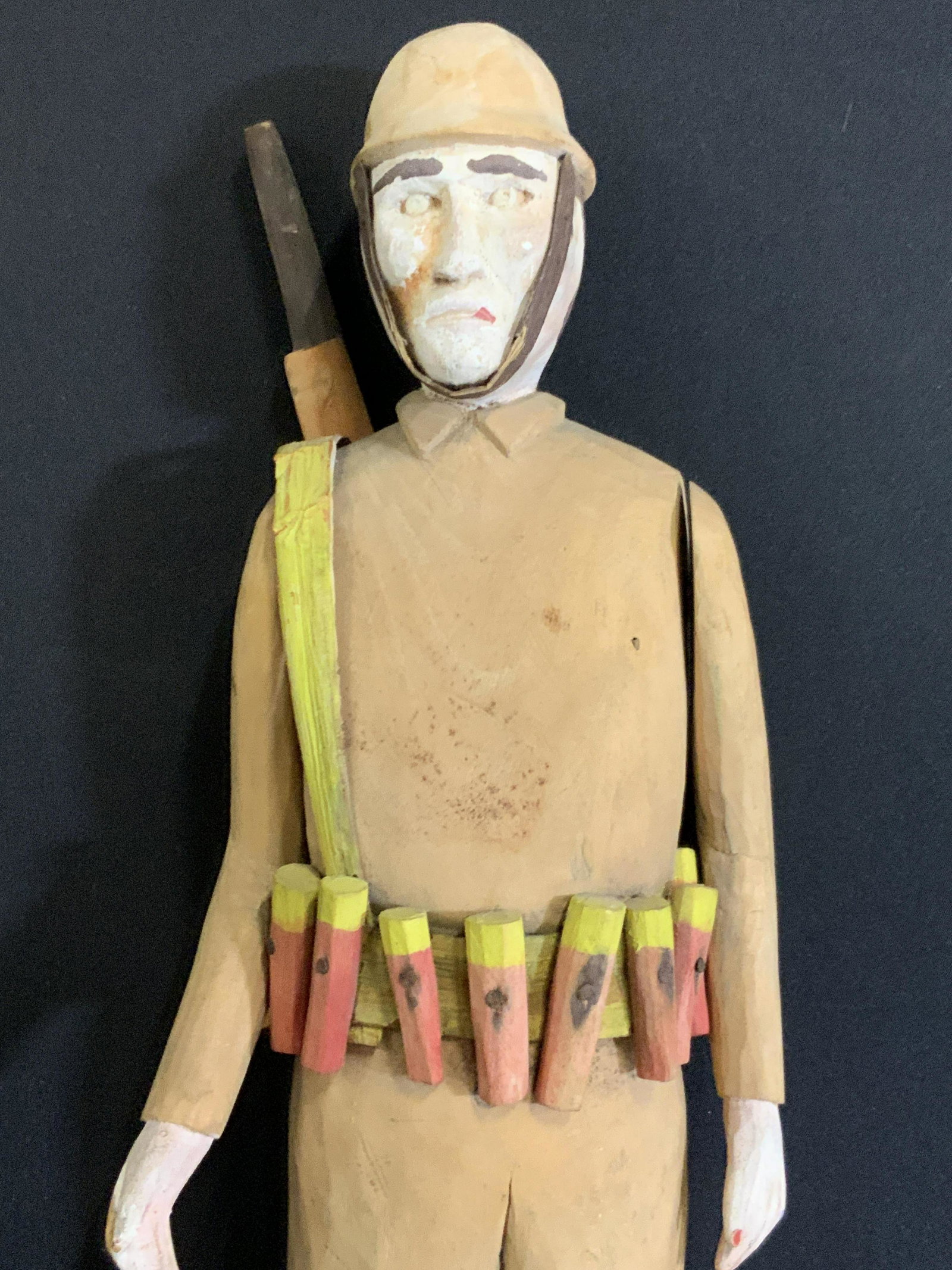 Antique Folk Art Handmade Wooden Soldier: Possibly antique hand carved wooden soldier. The soldier wears a light brown outfit, a hat, orange boots, and a utility belt stocked with ammunition. Over his shoulder he carries a gun that resembles 
