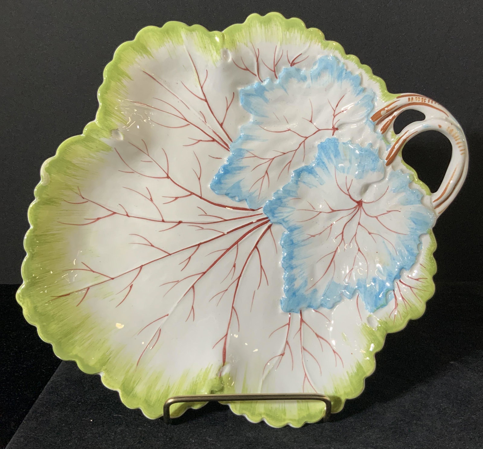 MOTTAHEDEH Italian Porcelain Leaf Form Dish: Hand painted dish in the shape of a leaf. The edges of the plate are scalloped to resemble a leaf edge. The handle is painted to resemble a leaf stem. The colors include vibrant blues, reds, browns, a