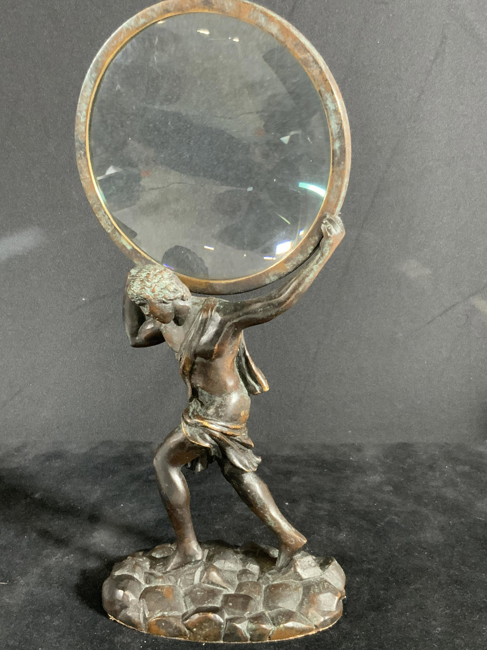 MAITLAND SMITH Bronze God Atlas Standing Magnifier: A vintage bronze figural of the Greek God Atlas holding up a magnifying glass as he would be depicted holding up the world. Magnifying glass is clear, no cracks. Some patina on Atlas. Underside has so