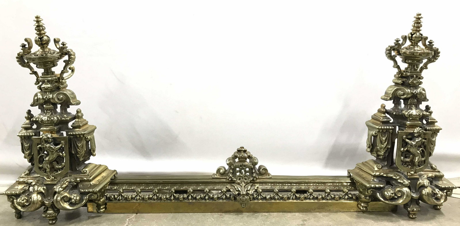 Vintage Brass Andiron Fender: Andirons attach to fender area to make 1 long piece. Each area of piece is gold toned brass & ornate. Andirons can be detached from center piece. Center of andirons have lion standing on hind legs det