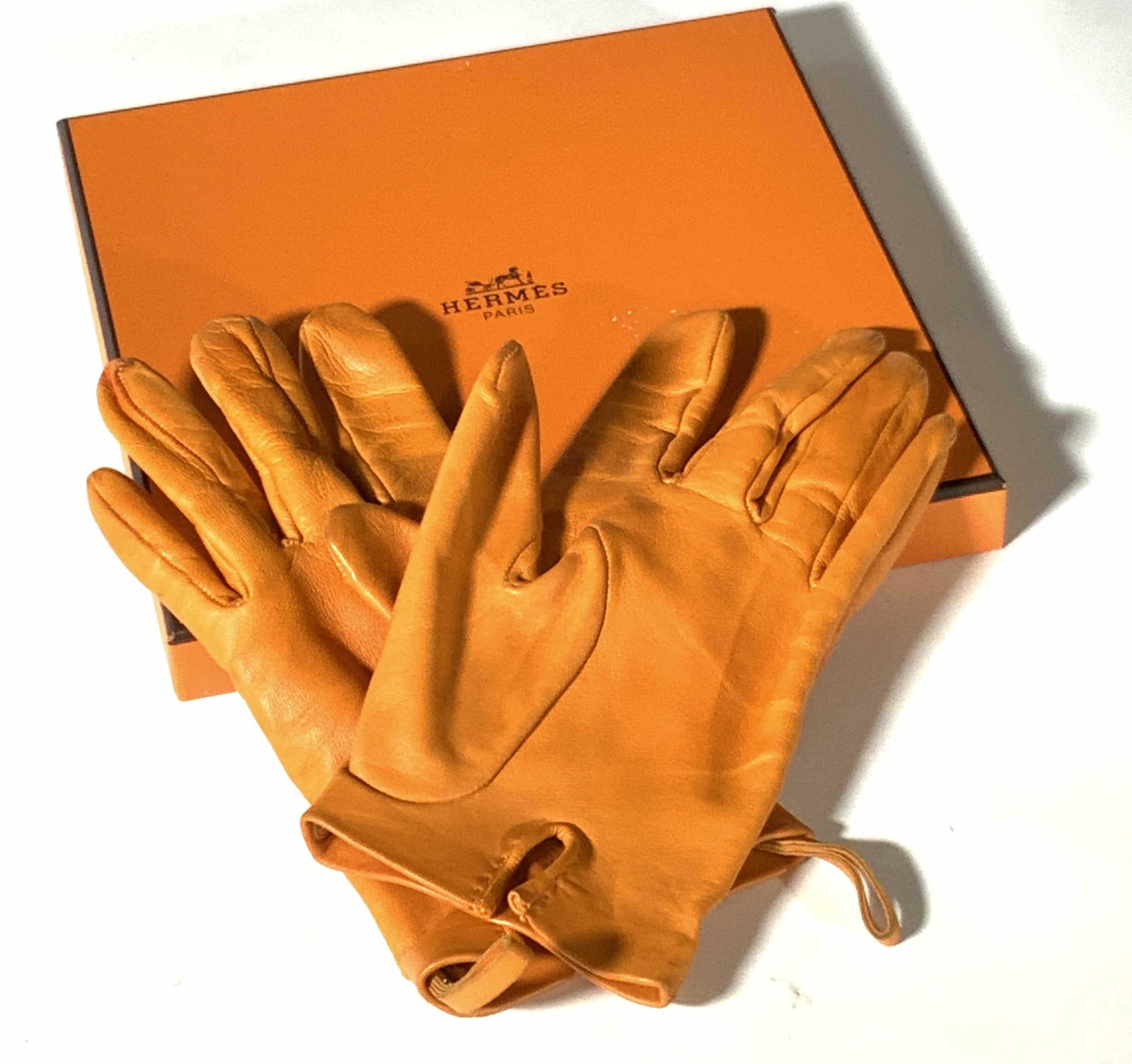 HERMÈS PARIS Orange Lambskin Gloves, Original Box: Orange lambskin gloves. Interior reads: 7 1/2. Made in France. Hermès Paris. Agneau/Lambskin. Slight discoloration on one glove. Interior also has silver tone snap buttons. Original orange Hermès bo