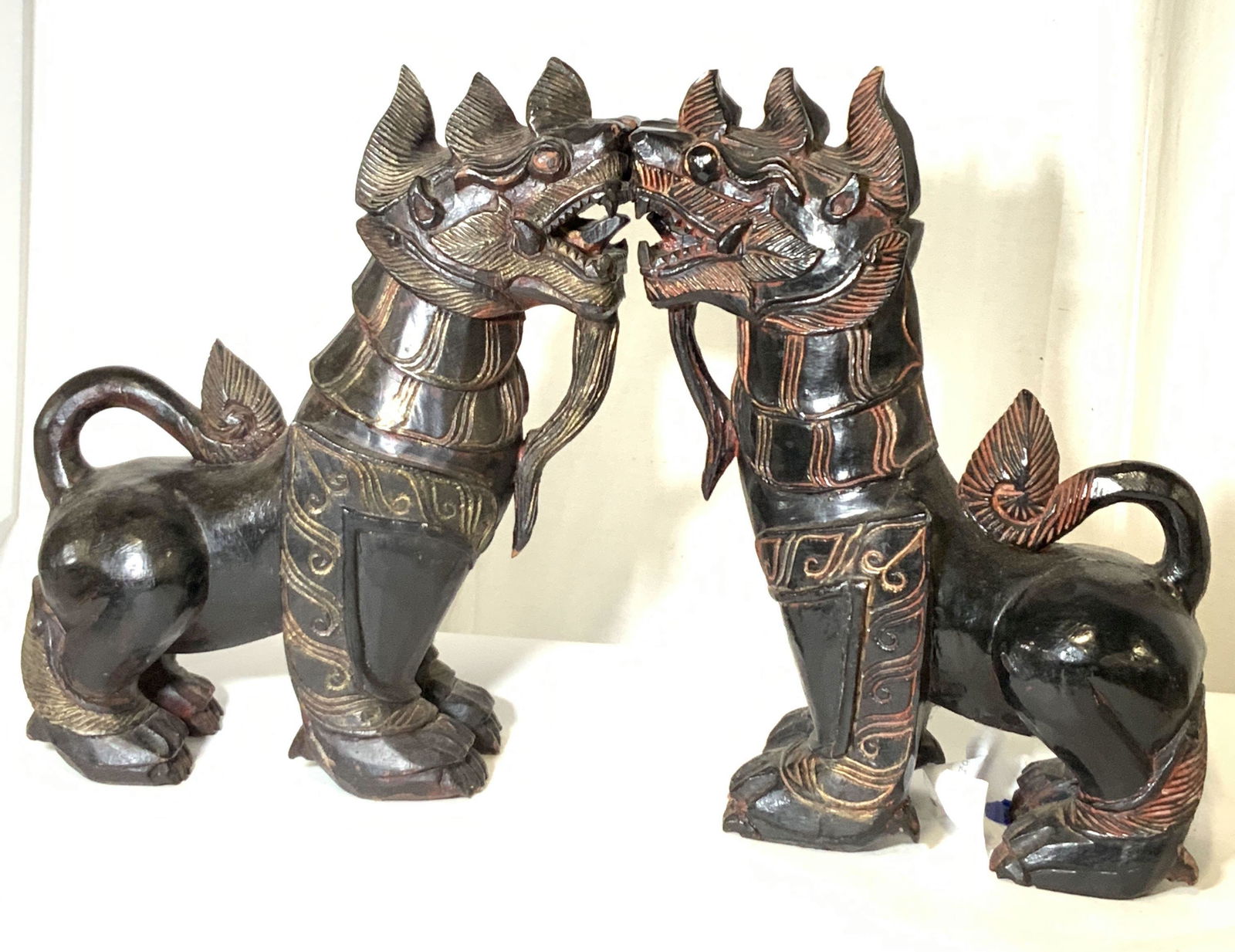 Pair Hand Carved Asian Temple Lion Sculptures: Pair of hand carved wooden Asian foo dogs / temple lion sculptures. Both are hand painted with black, red, and gilt. One lion is more red than the other. Lions have their mouths open, teeth & tongues