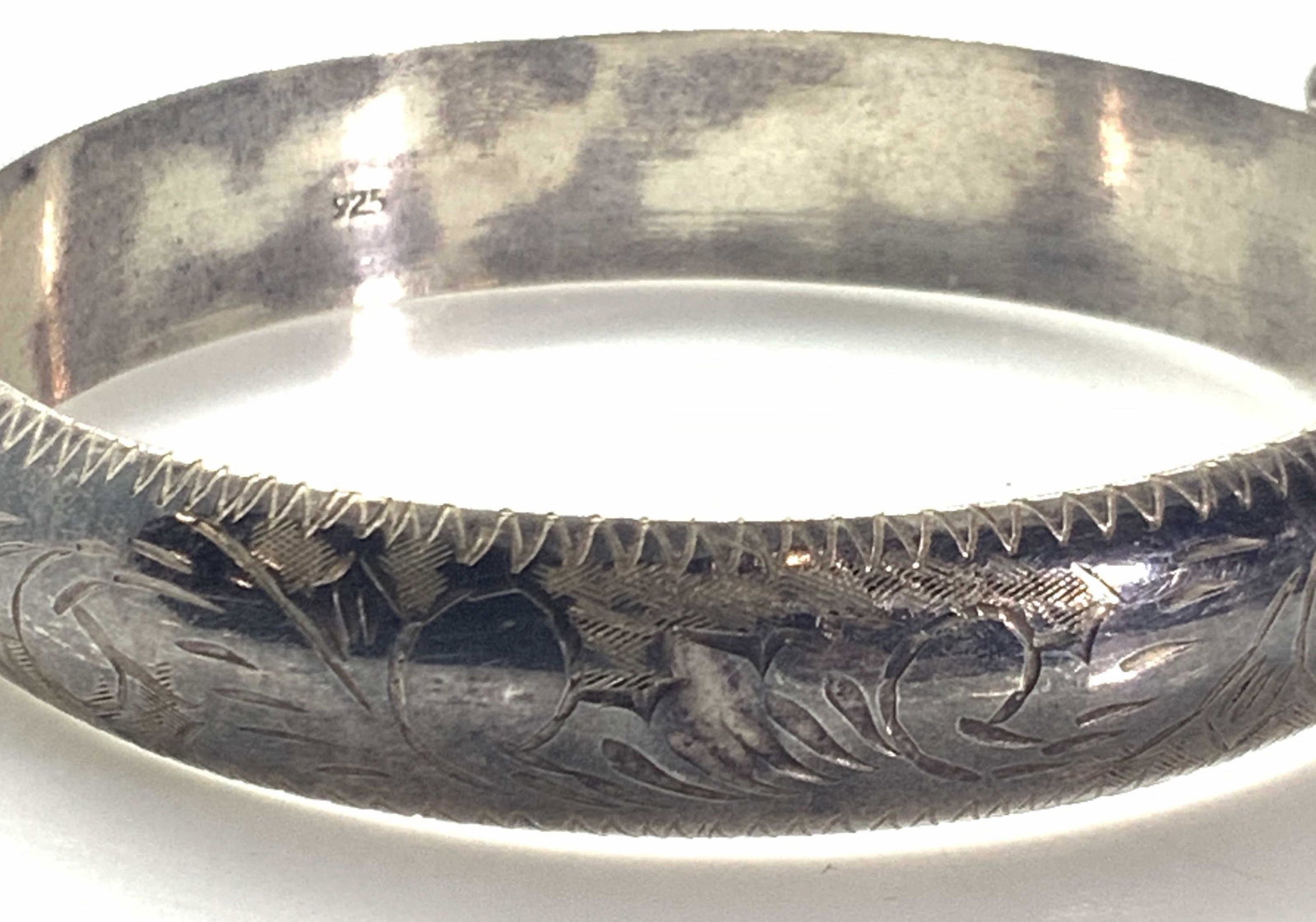 Vintage Sterling Silver Etched Bracelet, Jewelry: A sterling silver bracelet with etched detailing throughout. A small chain is affixed to bracelet. Small sawtooth design sits atop near chain. Underside is polished and marked 925. Approx. Diameter 2.